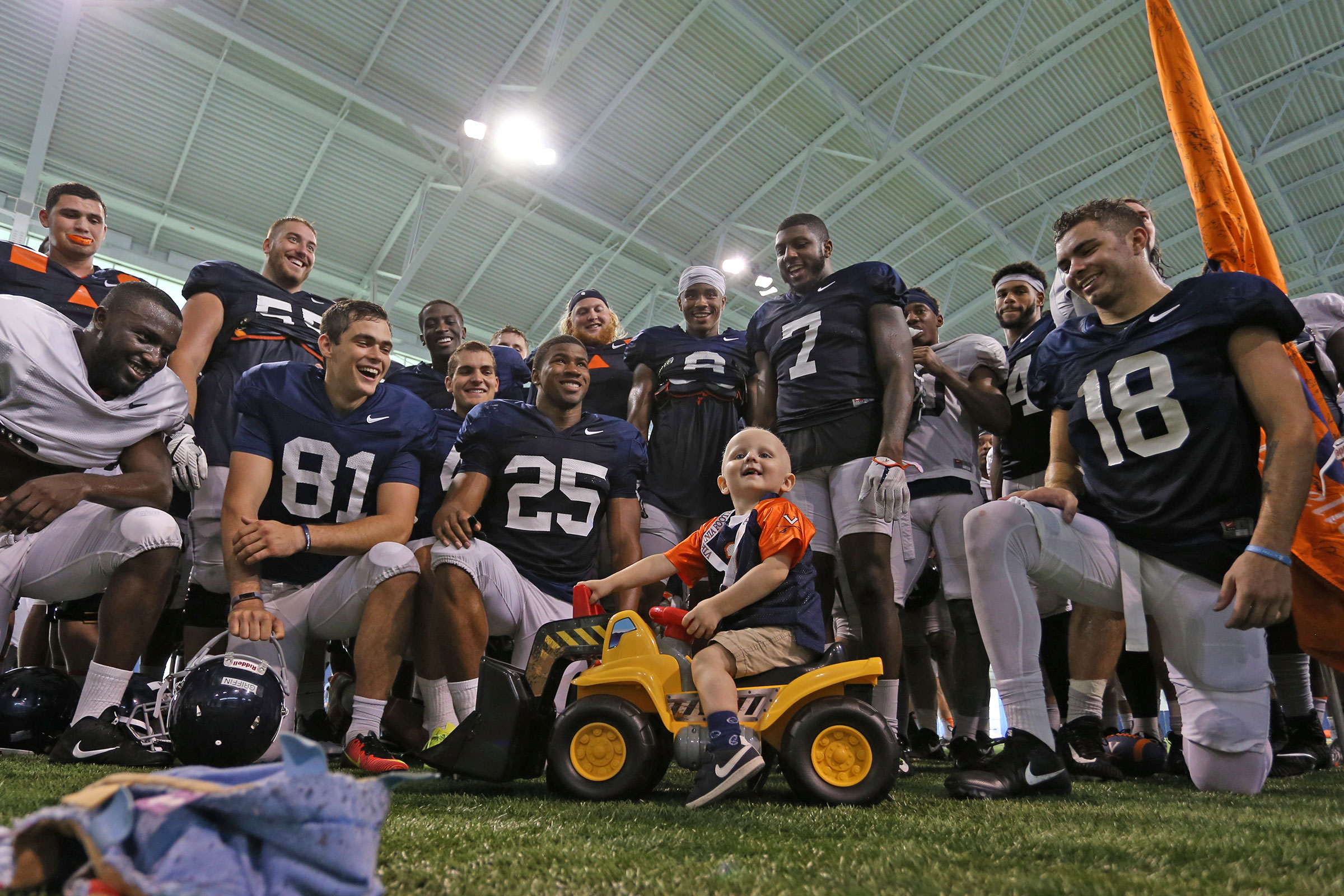 Luke Edwards sits on a little bull dozer while being surrounded by the UVA football team