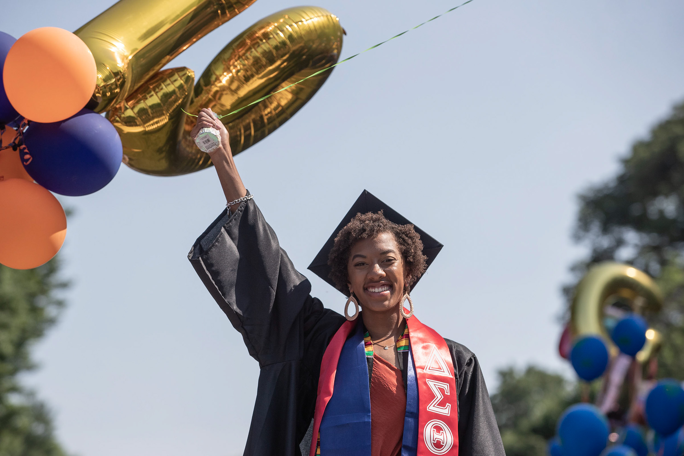 Graduate with right arm raised holding golden balloons