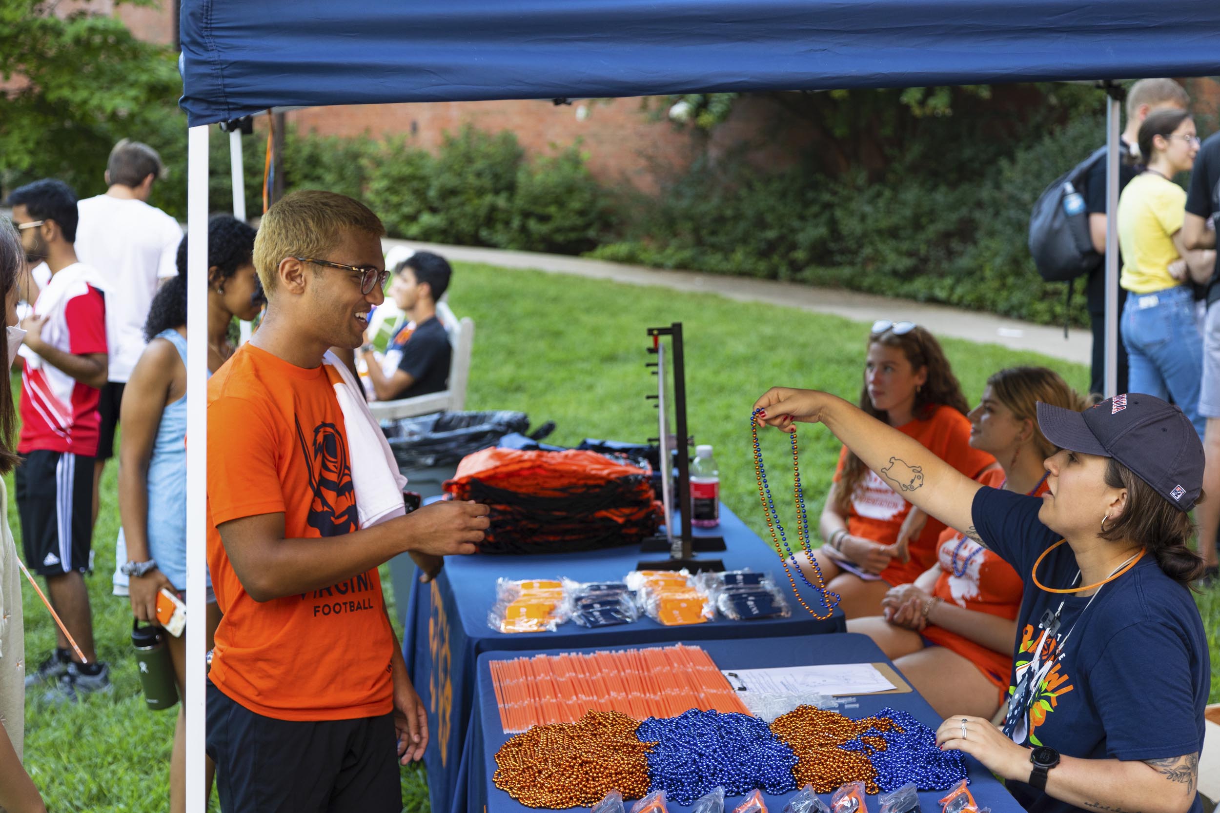 Student standing at a table of free UVA swag being handed blue and orange beads