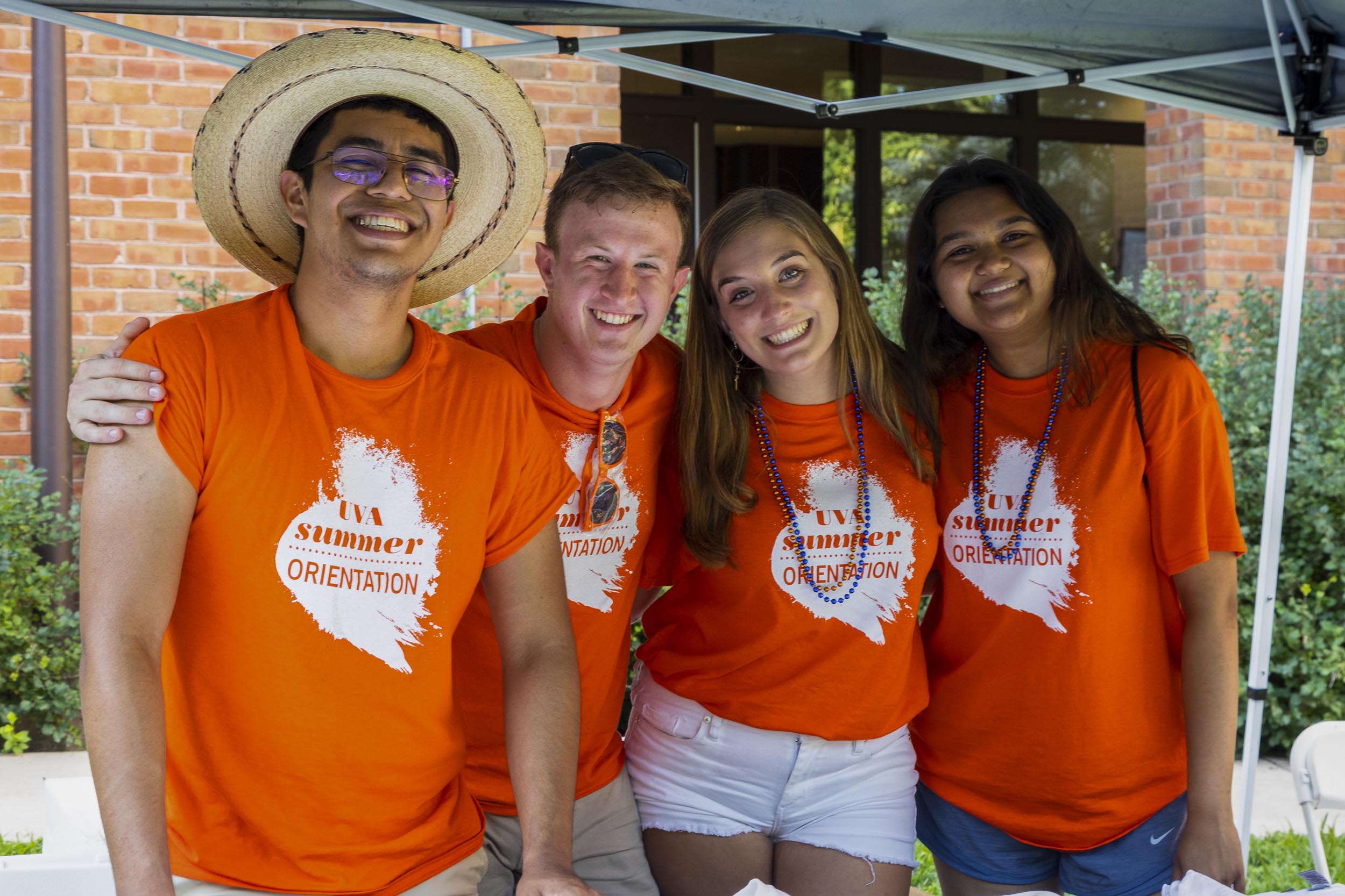 Four students holding each others shoulders for a picture wearing matching shirts that read: UVA Summer Orientation