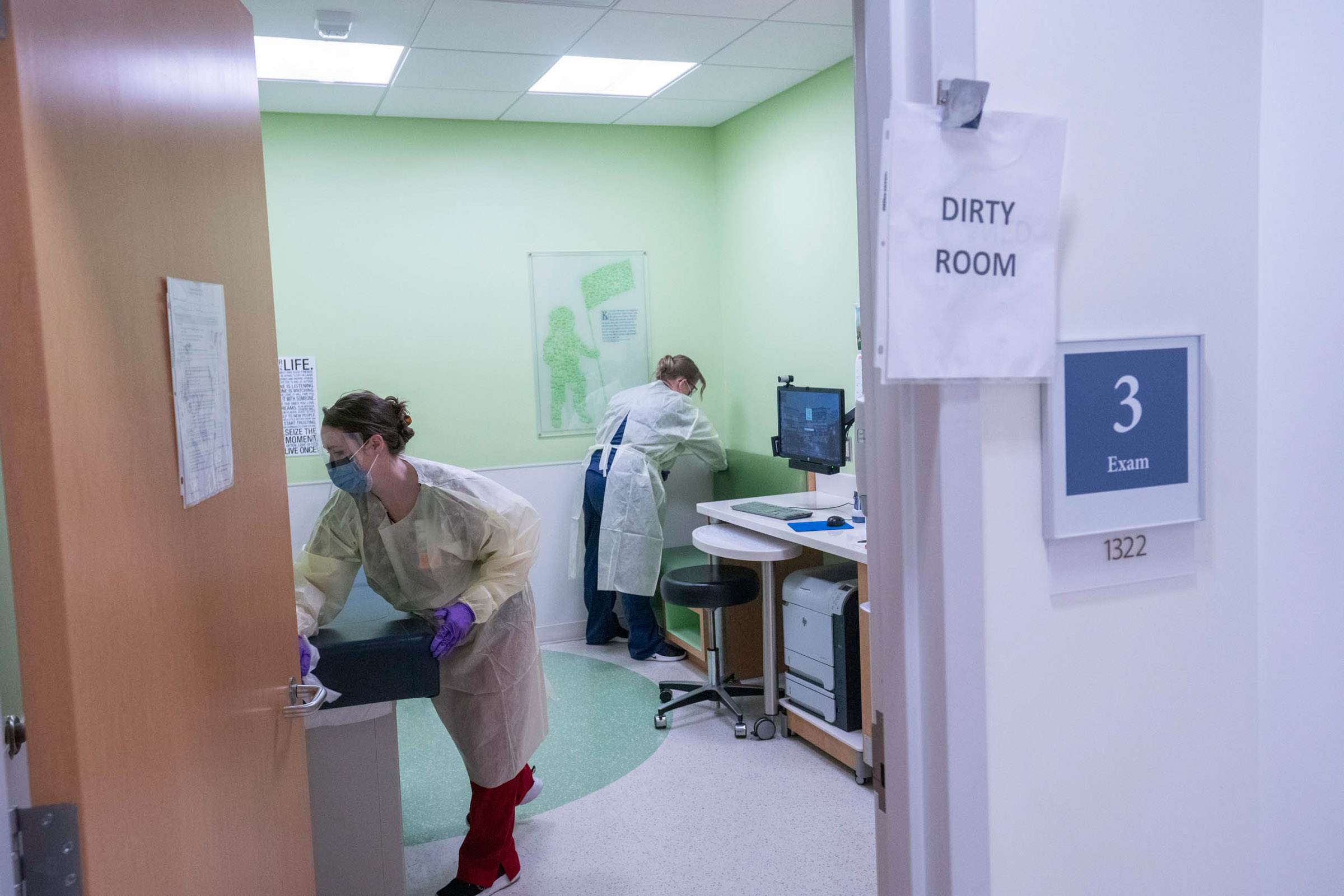 Healthcare professional cleaning an exam room with a sign on the door that reads dirty room