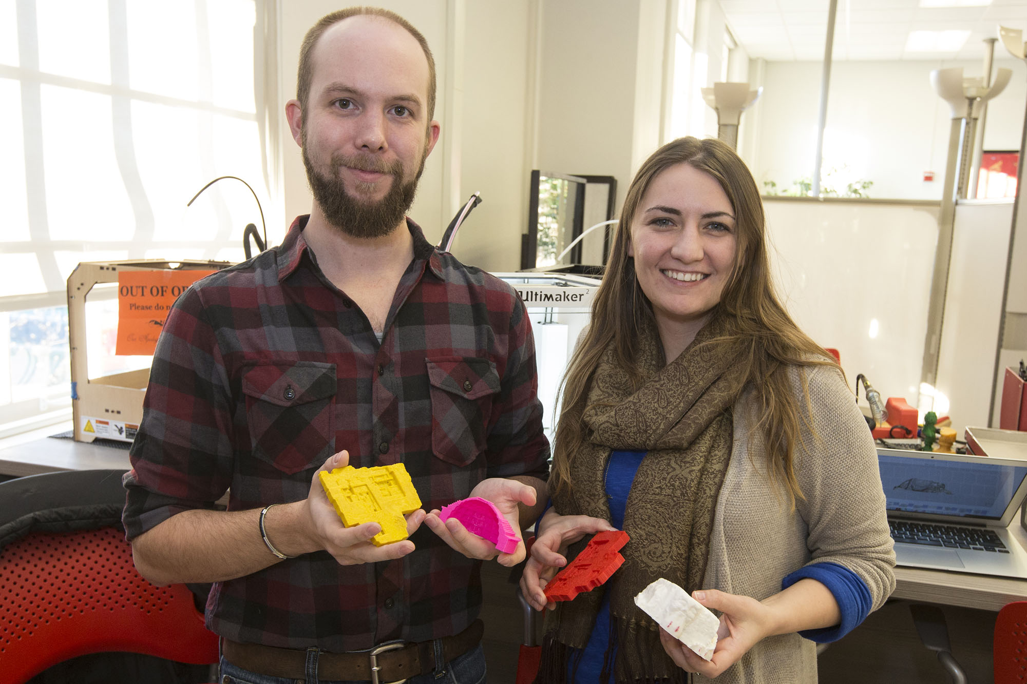 Graduate students Jennifer Grayburn and Benjamin Gorham hold examples of artifacts and archaeological dig sites they’ve recreated using the 3-D printer.