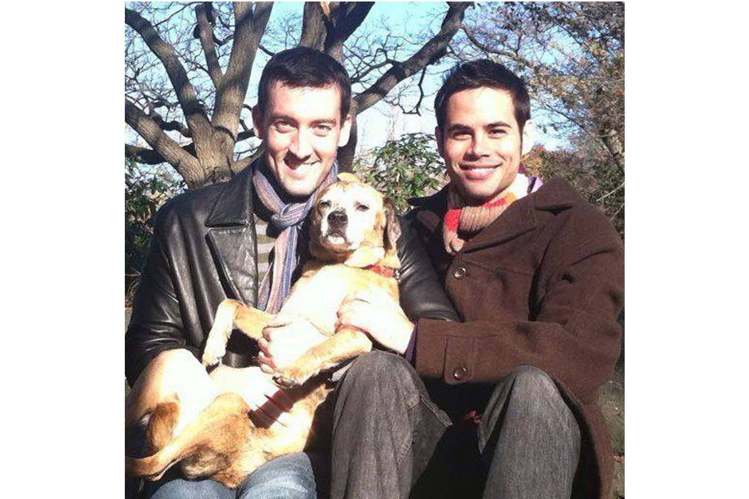 Kent and chase hold their dog as they smile at the camera