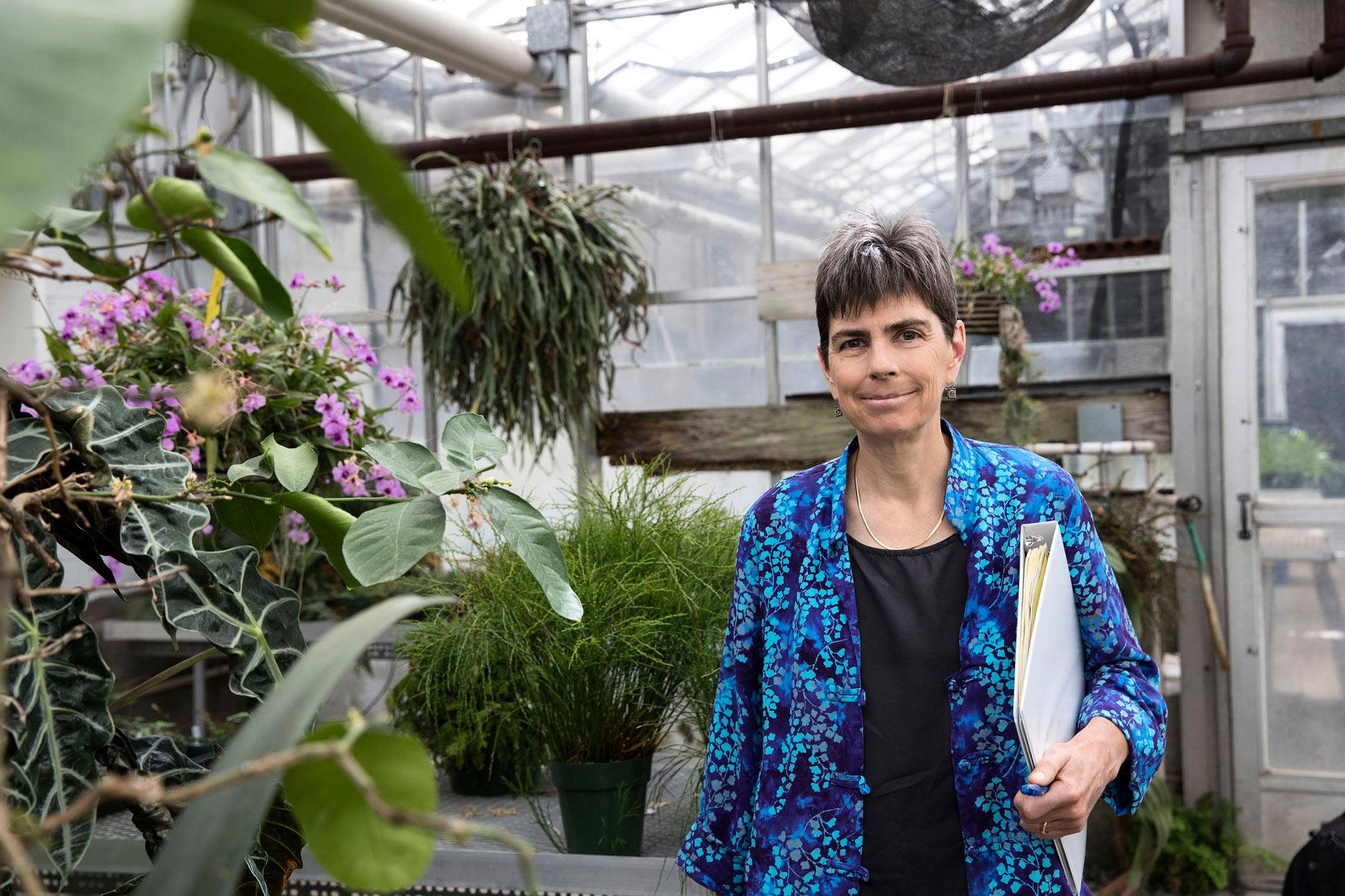 Laura Galloway, stands inside of a green house with flowers
