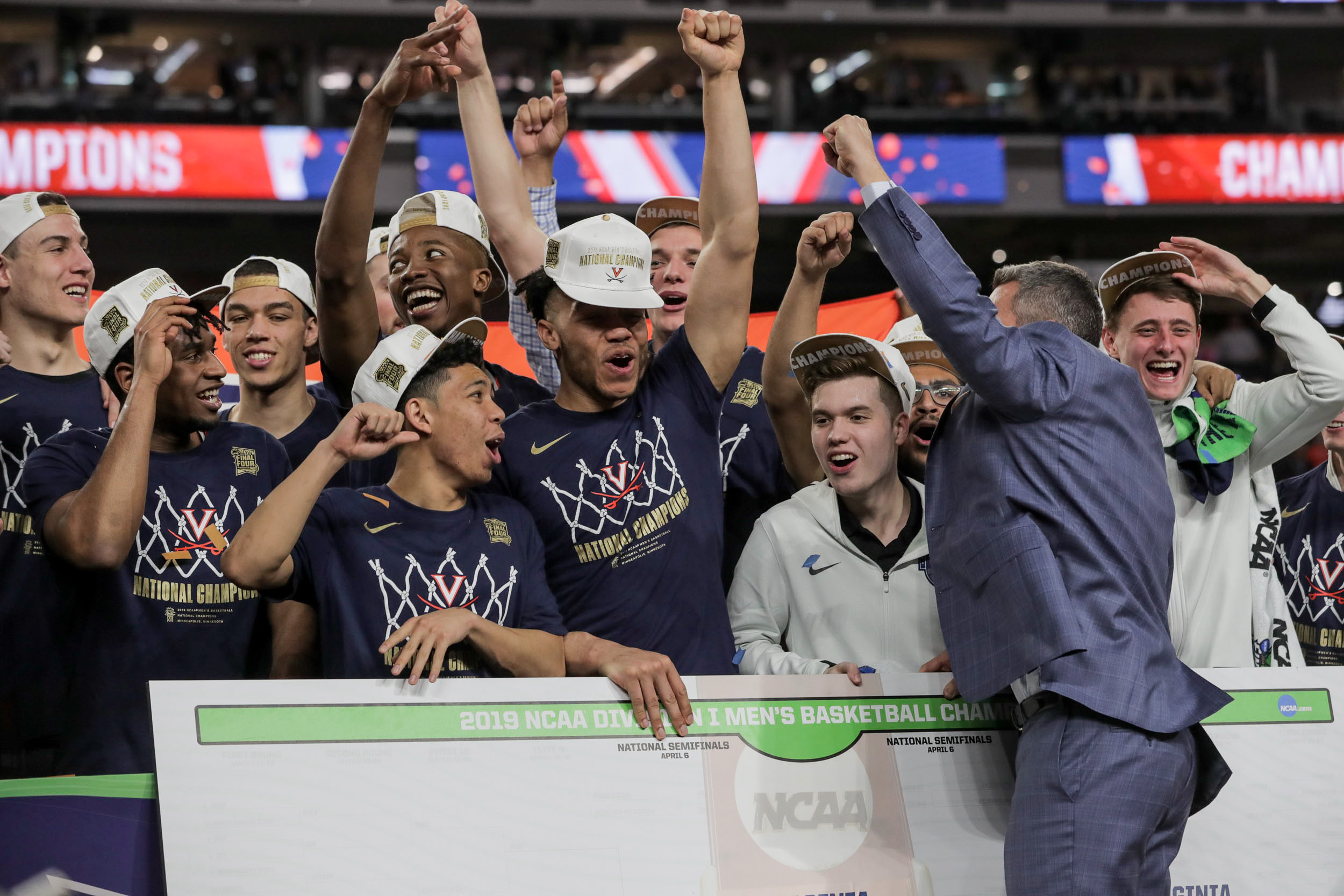 Basketball Team holds large check with Tony Bennett and all of them are cheering and raising their hands