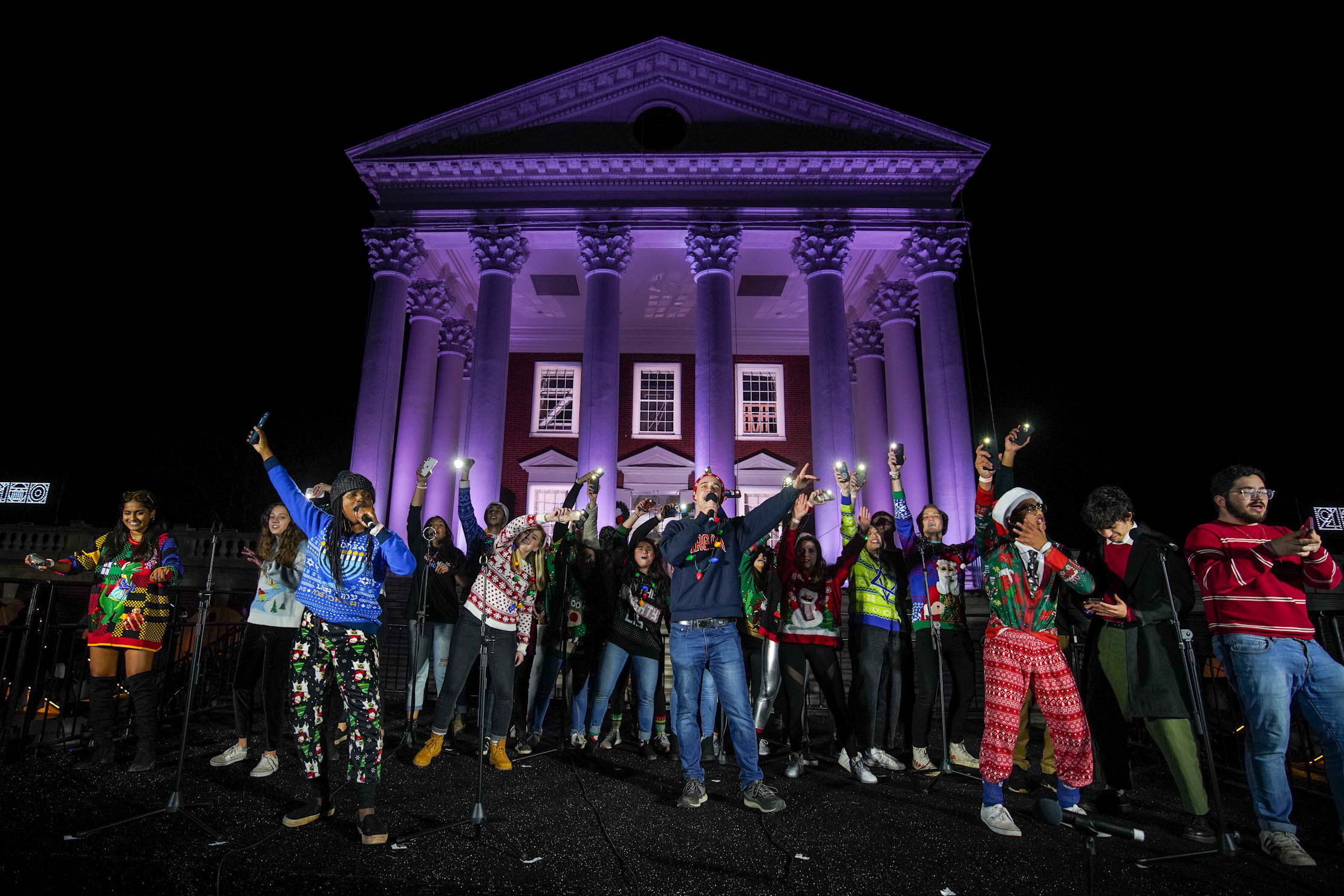 UVA's No tones singing group stands in front of the Rotunda illuminated in purple lights signing to a crowd