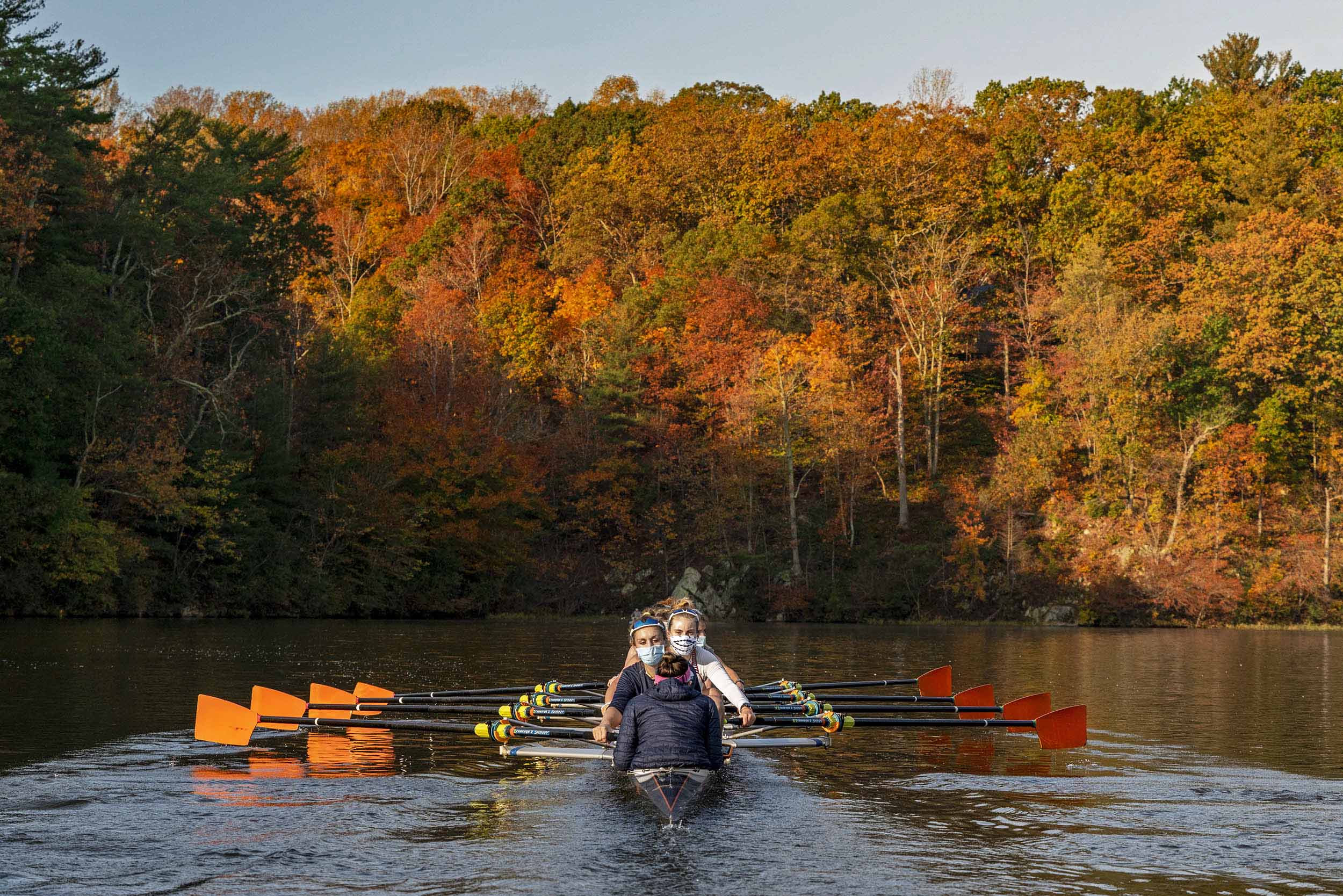 UVA Rowing team on a river surrounded by orange, yellow, and green trees