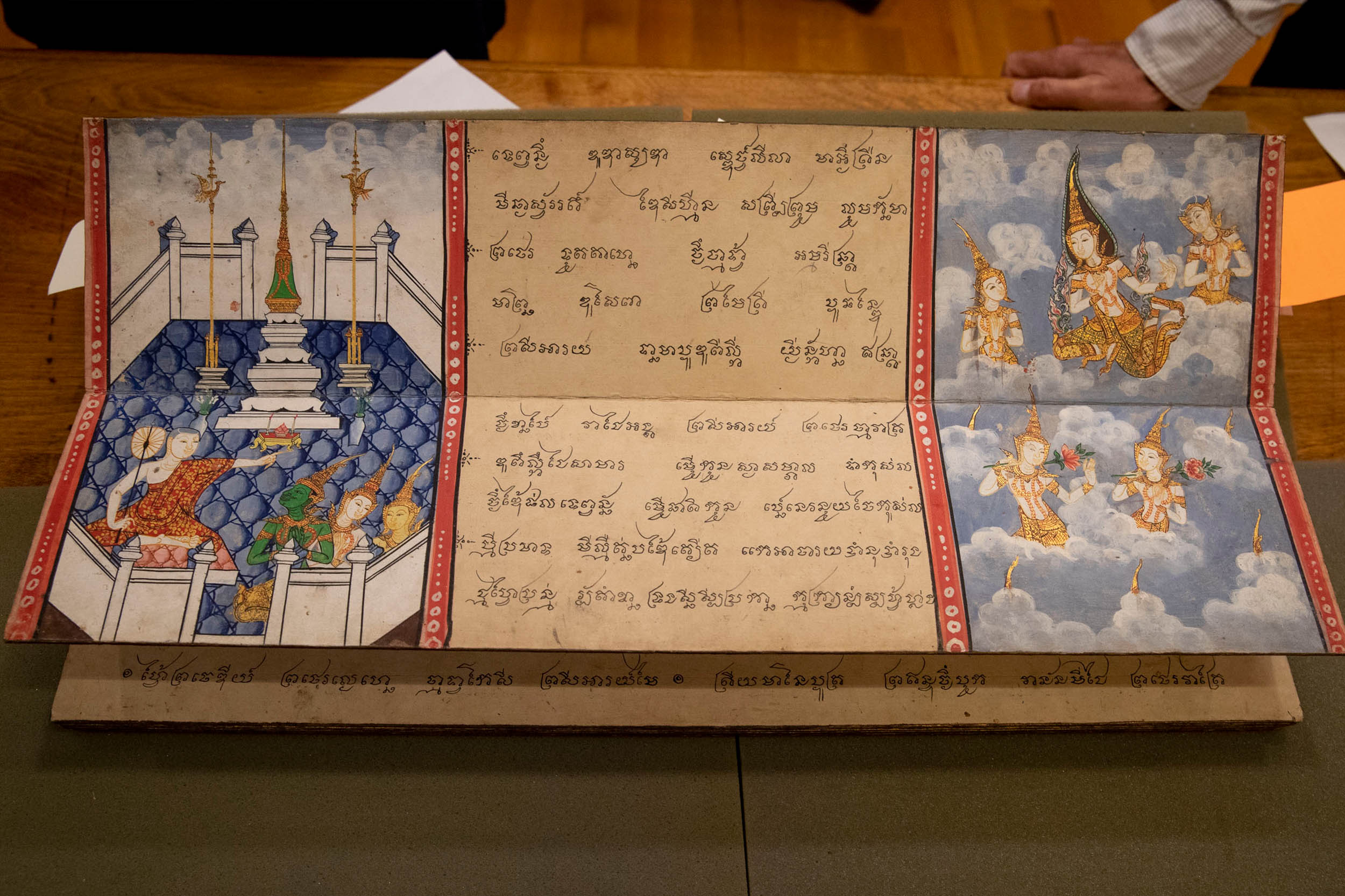 a book that folds out.  Left: Monks sitting on the floor of a temple  Middle: Text in a foreign language right: Monks on clouds in the air