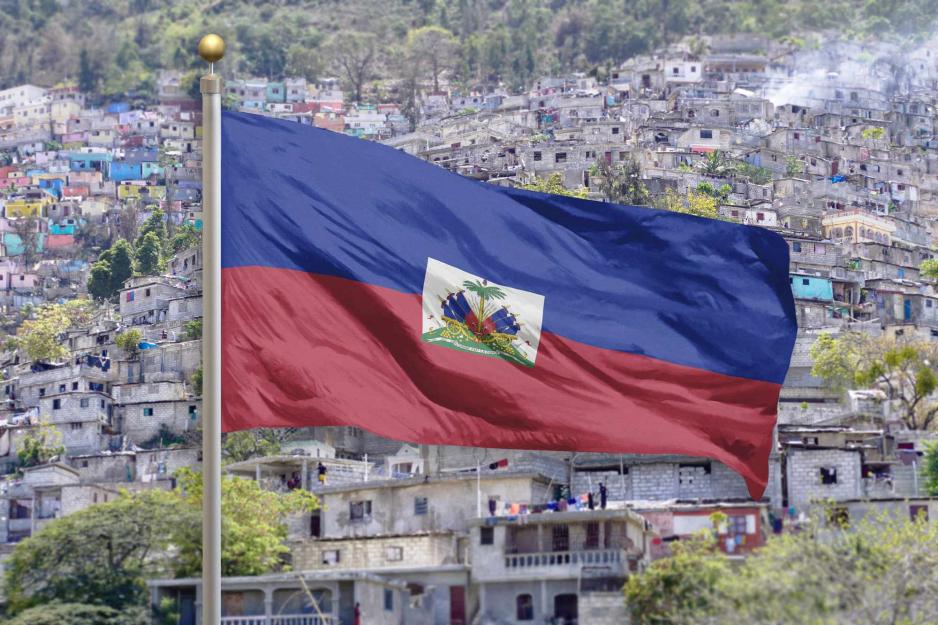 Illustration of Haiti flag waving against a backdrop of houses on a hillside.