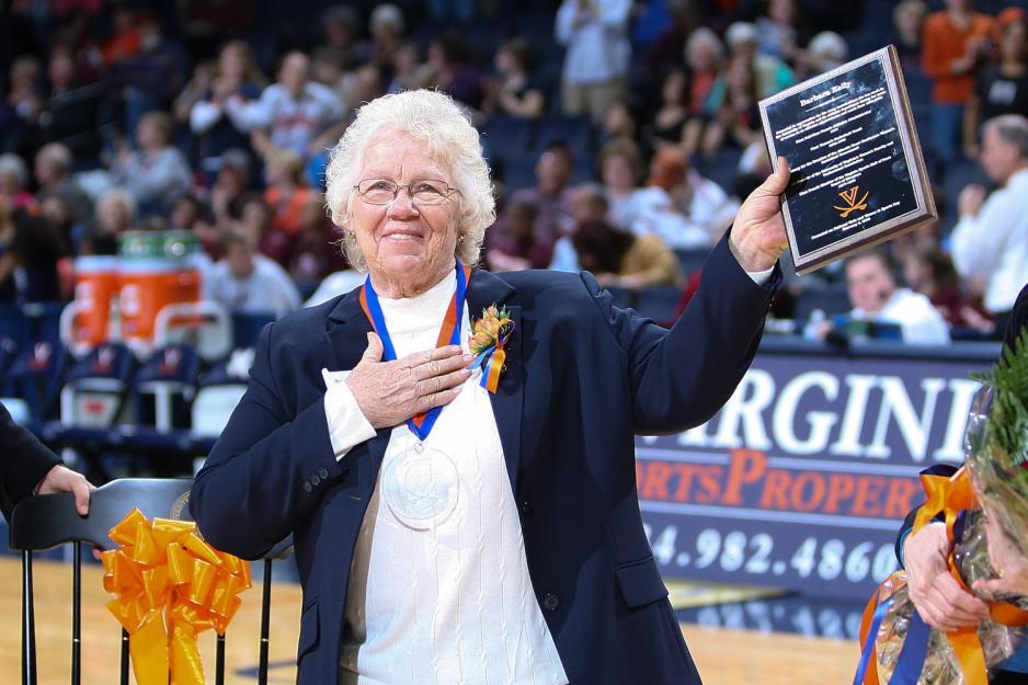 Barbara Kelly holds a plaque while wearing a medal standing on the basketball court
