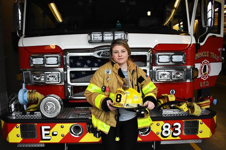 Alice Thomson wearing her firefighter jacket holding her helmet in front of fire engine 83