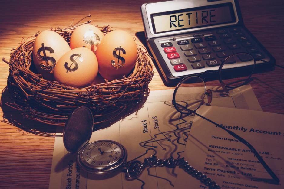 Table with a nest with eggs in it with dollar signs on the egg, a calculator that reads retire, papers and a stop watch