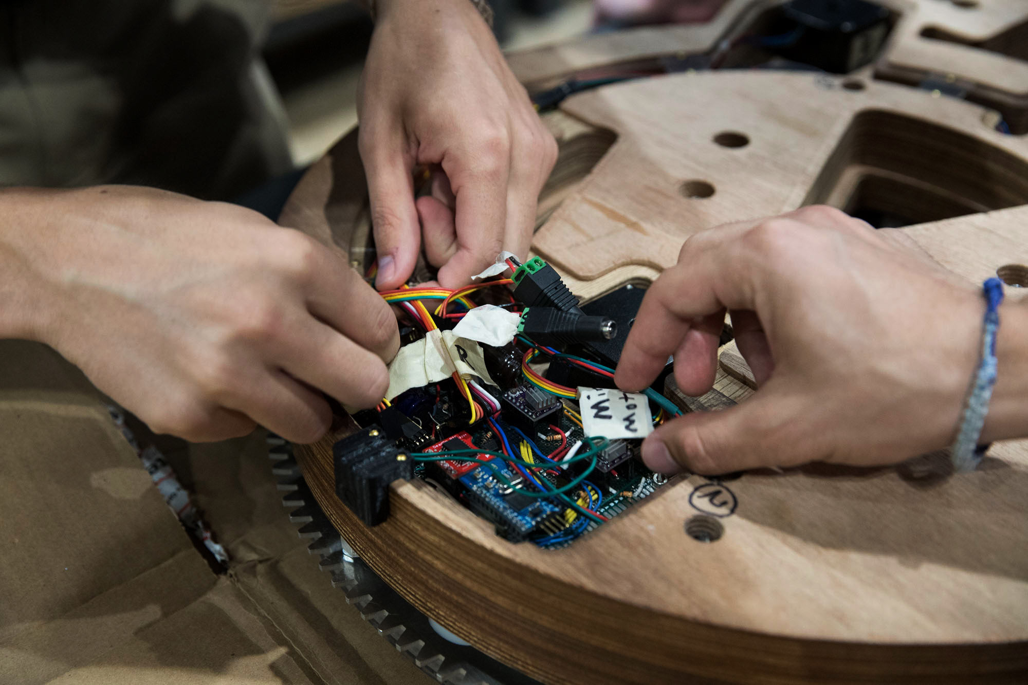 Hands placing electronics in the back of an unfinished wooden clock