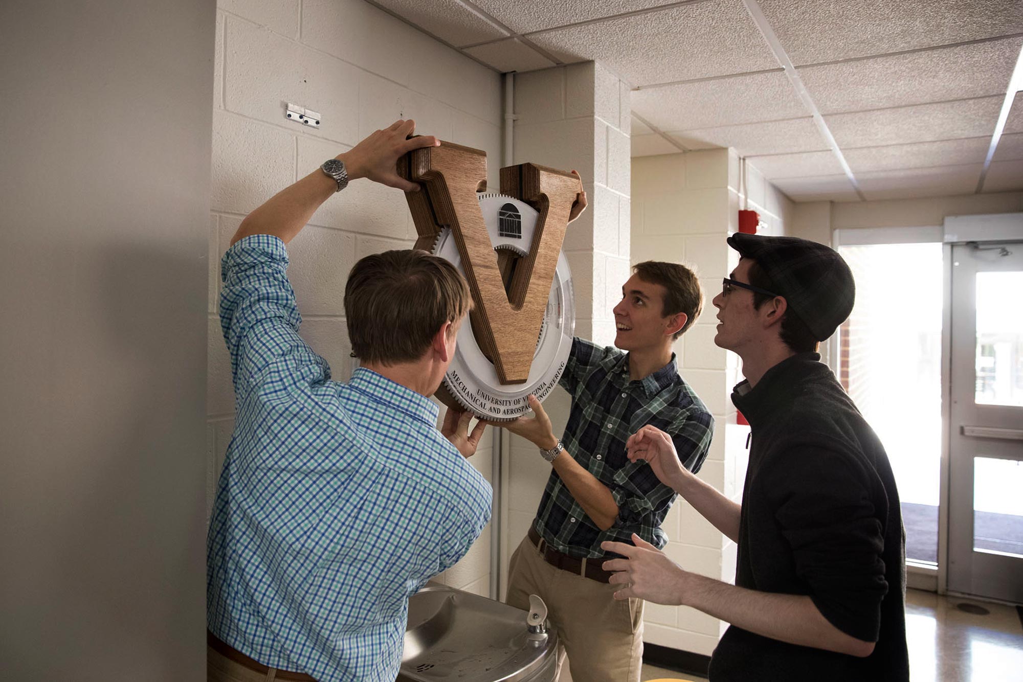 Three students hanging a clock in a hallway over a waterfountain