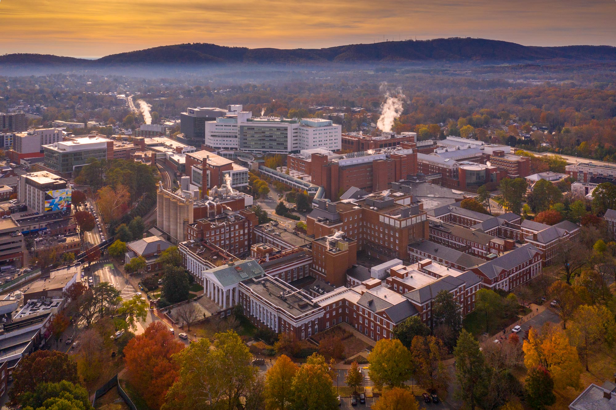 Arial view of the UVA Health Center Buildings with an orange and yellow sunset just above the blue ridge mountains