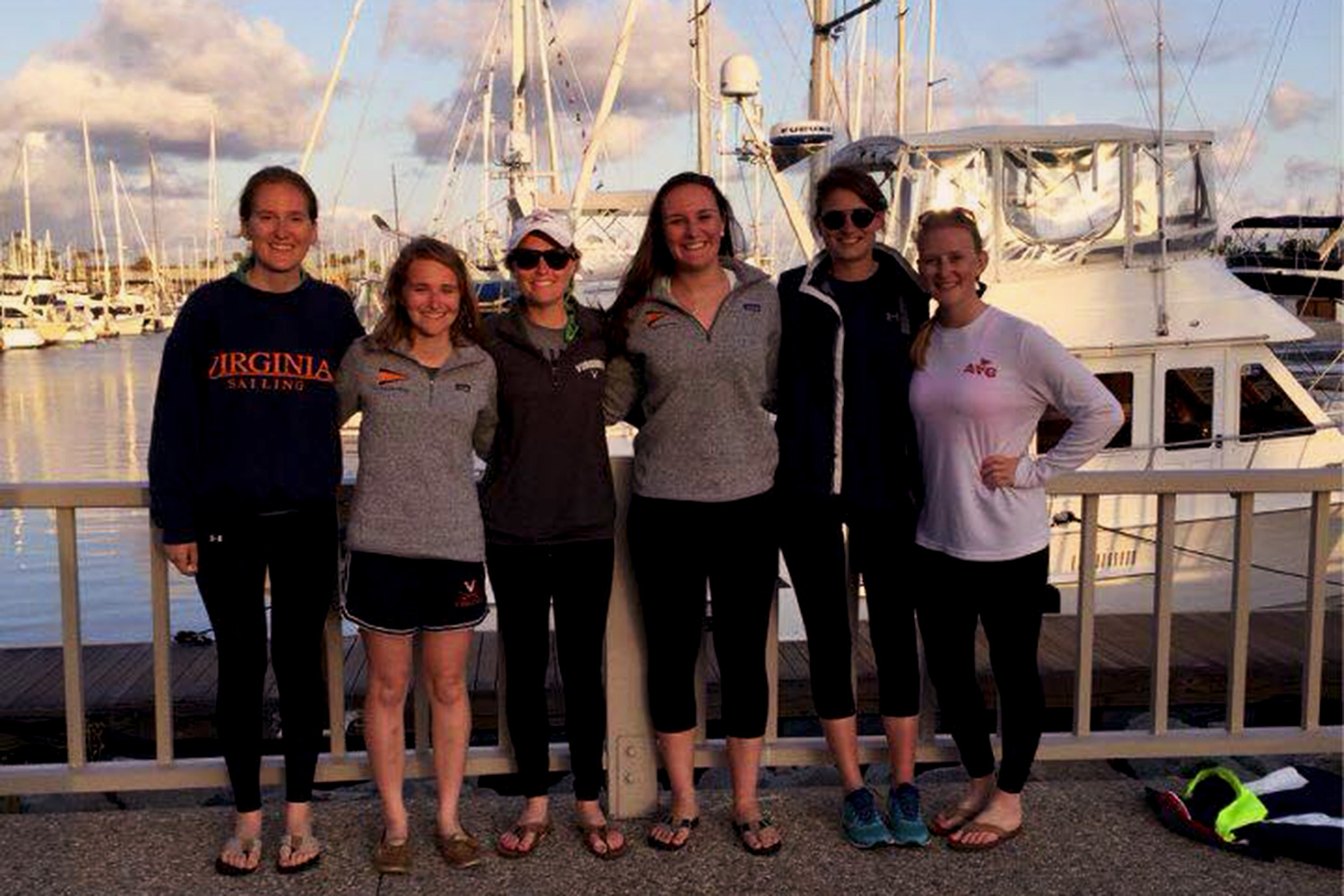 UVA women's sailing team stand on the dock smiling at the camera