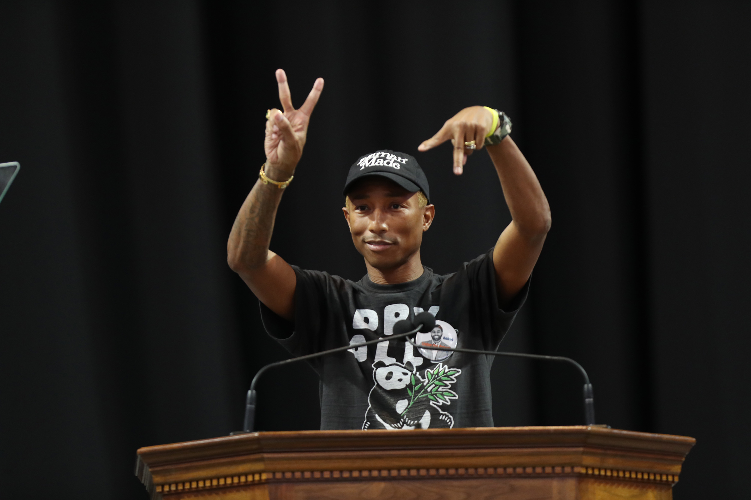 Pharrell Williams gives peace sign with right hand and two fingers down with left hand from the podium