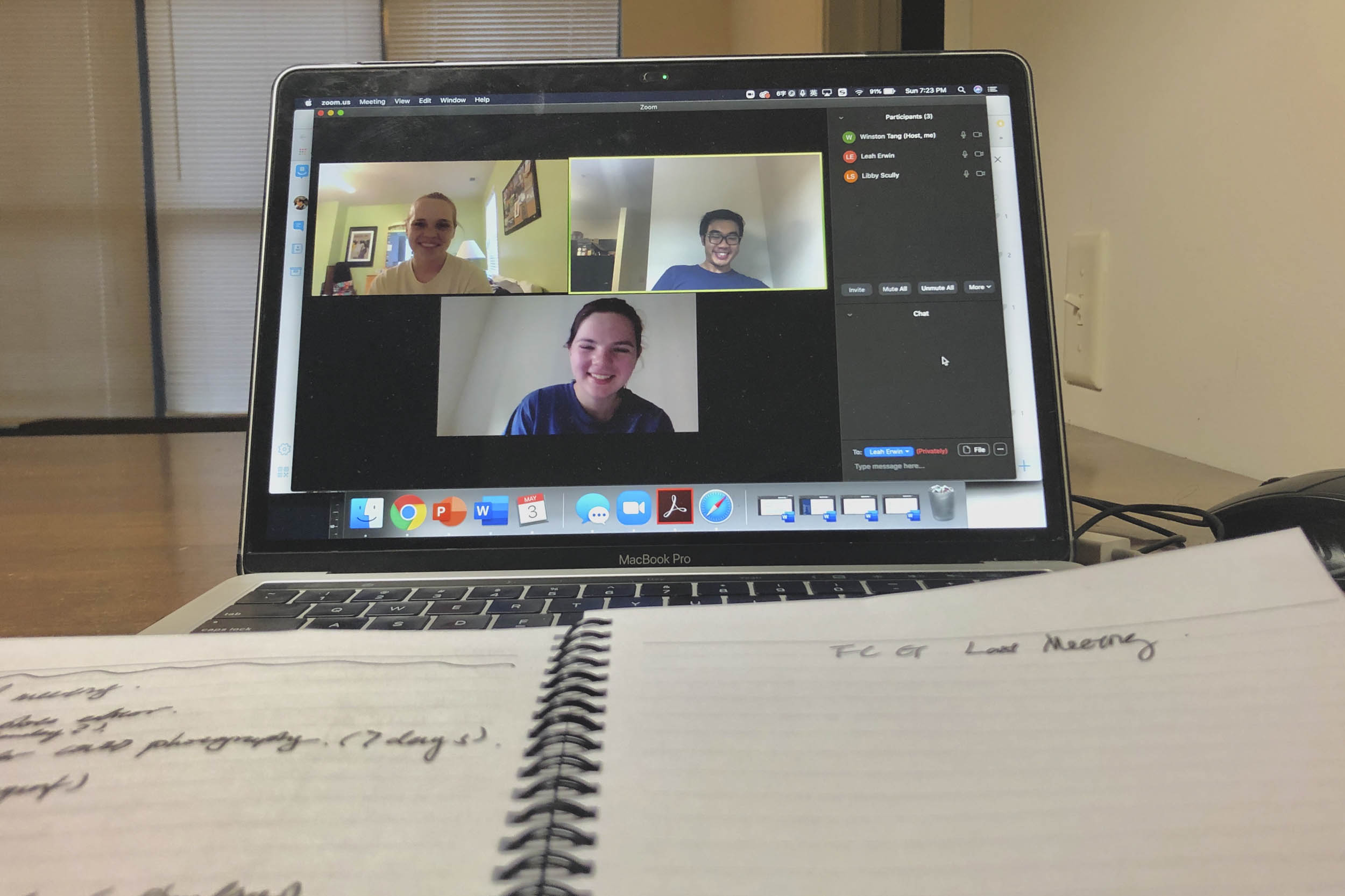 Notebook laying on a laptops keyboard while a zoom meeting is on the screen with 3 attendees