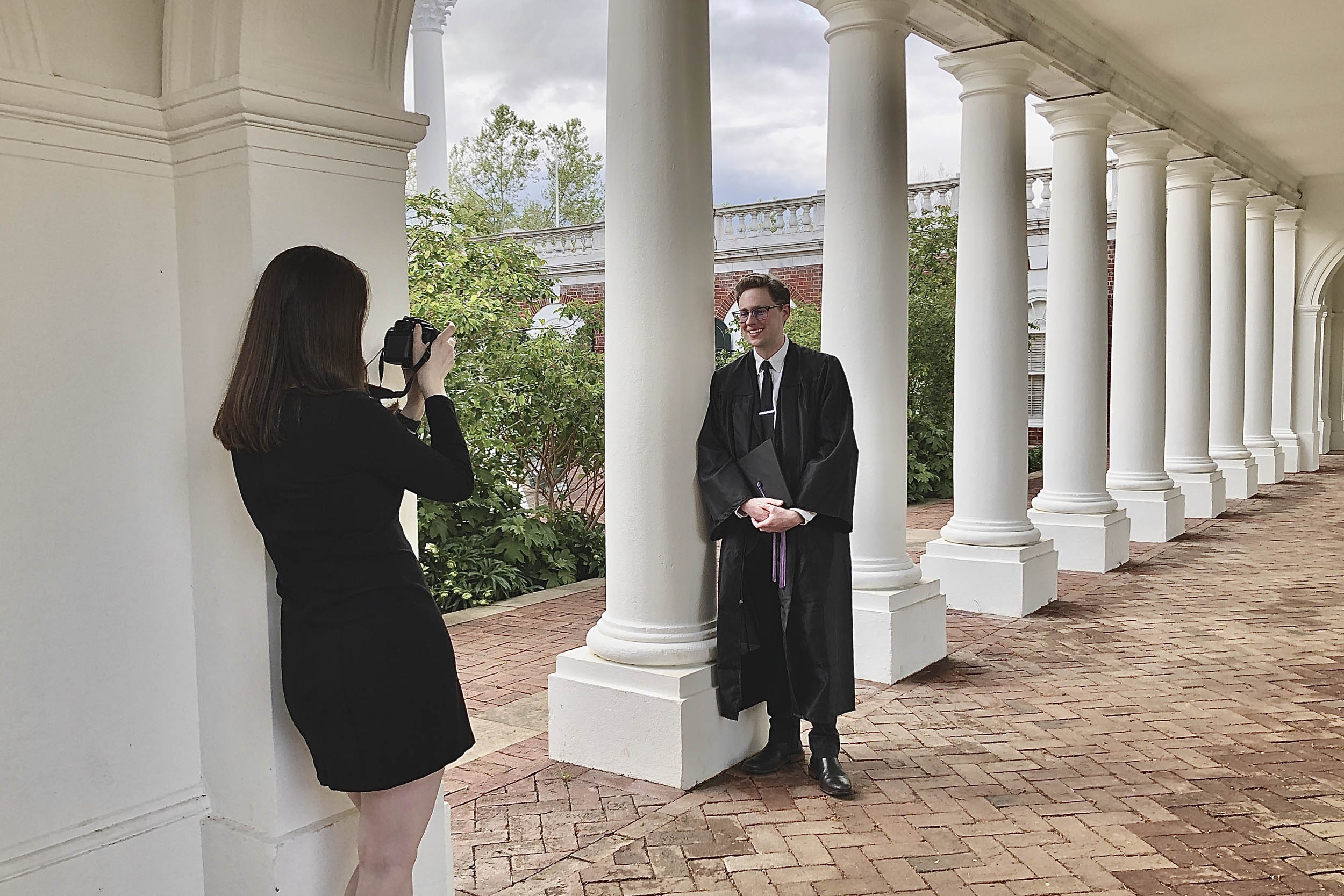 Woman taking a picture of a graduate leaned up against a white column