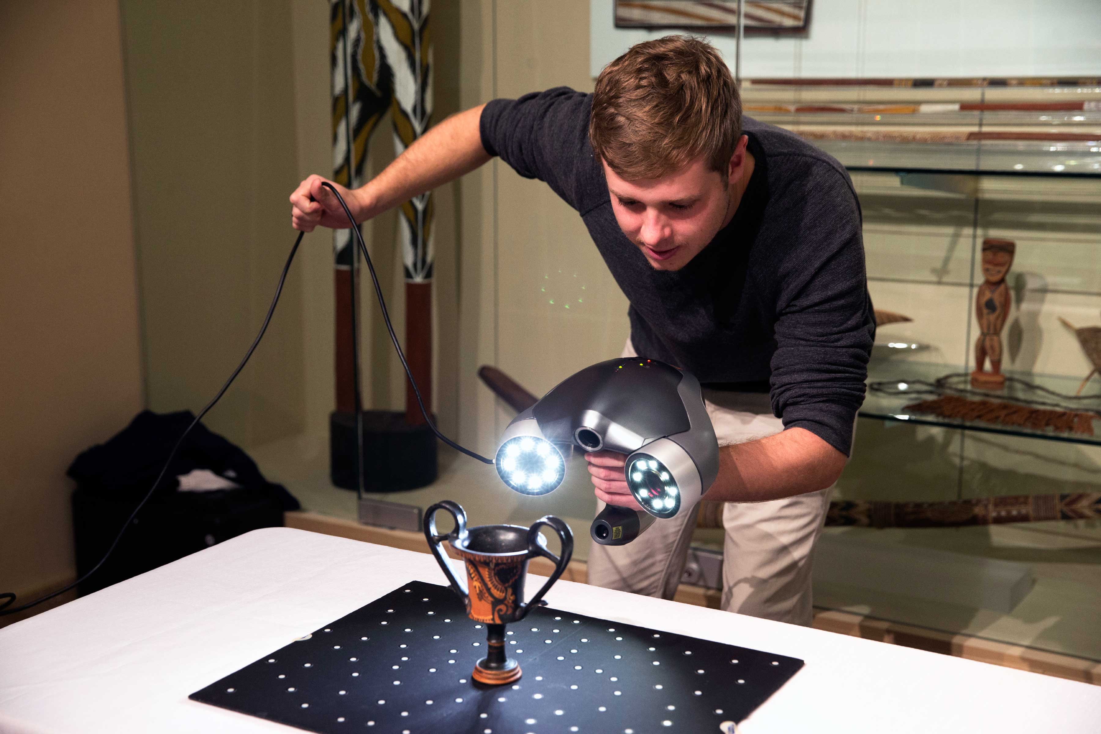 Lewis aims a 3-D scanner at a fourth-century vase atop a reflective mat that provides reference points for the scanner to build a virtual 3-D space. (Photo by Dan Addison, University Communications)