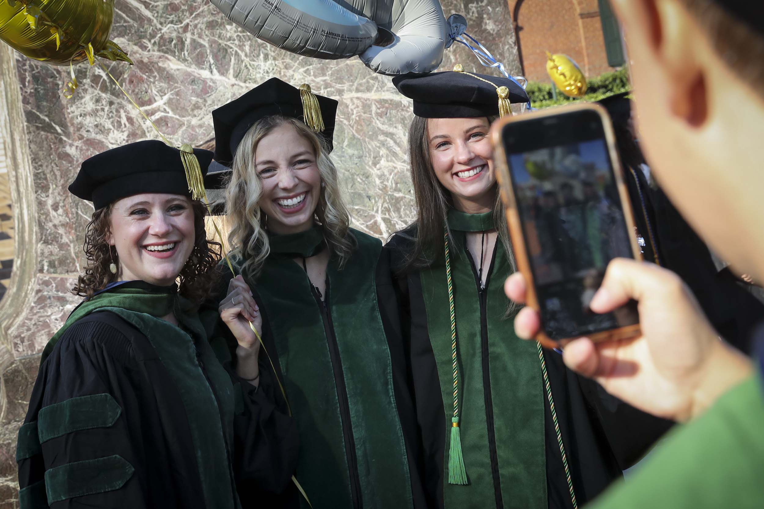 Graduate taking a picture of three other graduates on their phone