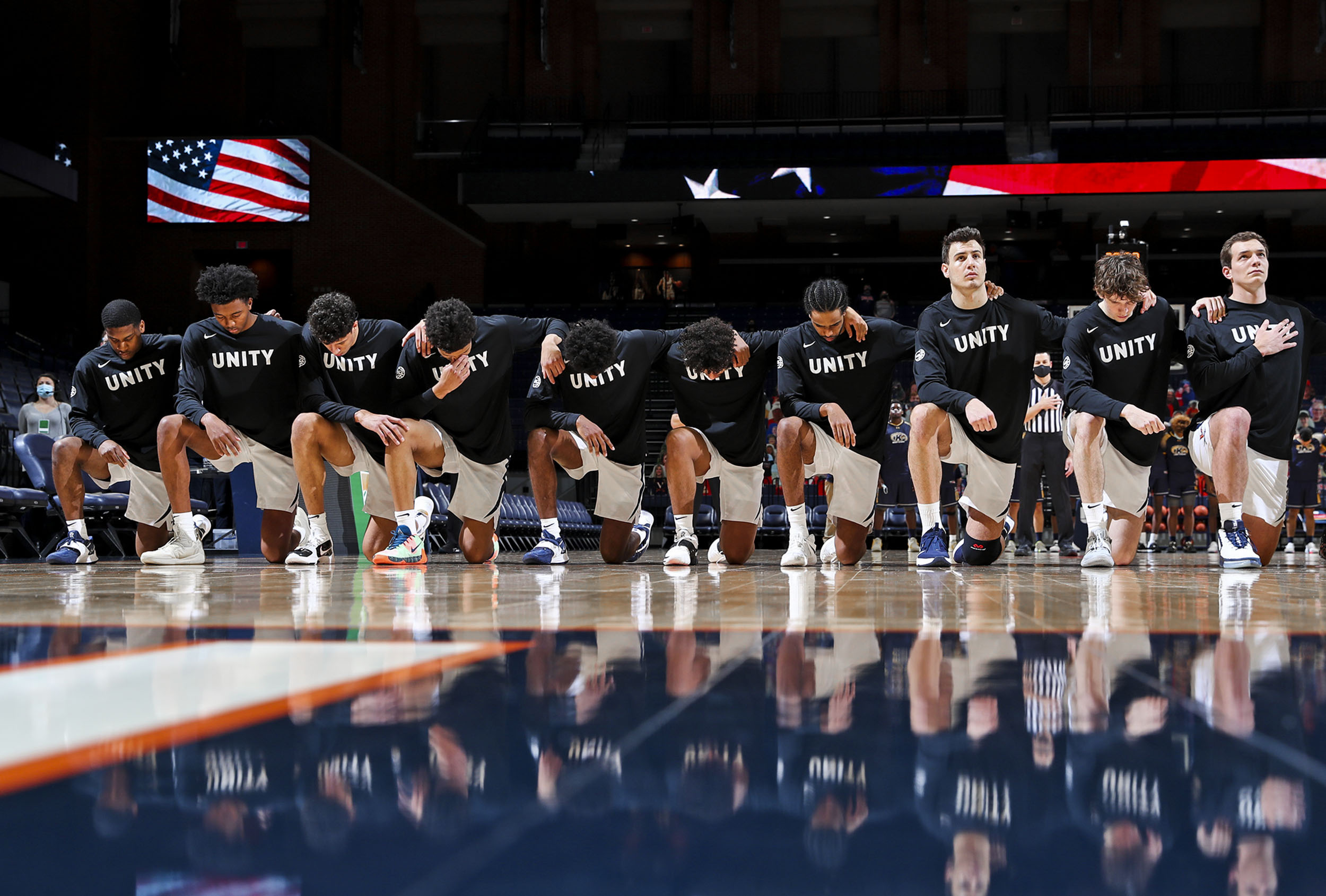 UVA mens basketball team kneel doing the national anthem while bowing their heads except the last player in line(right), he is kneeling but head raised and hand over heart