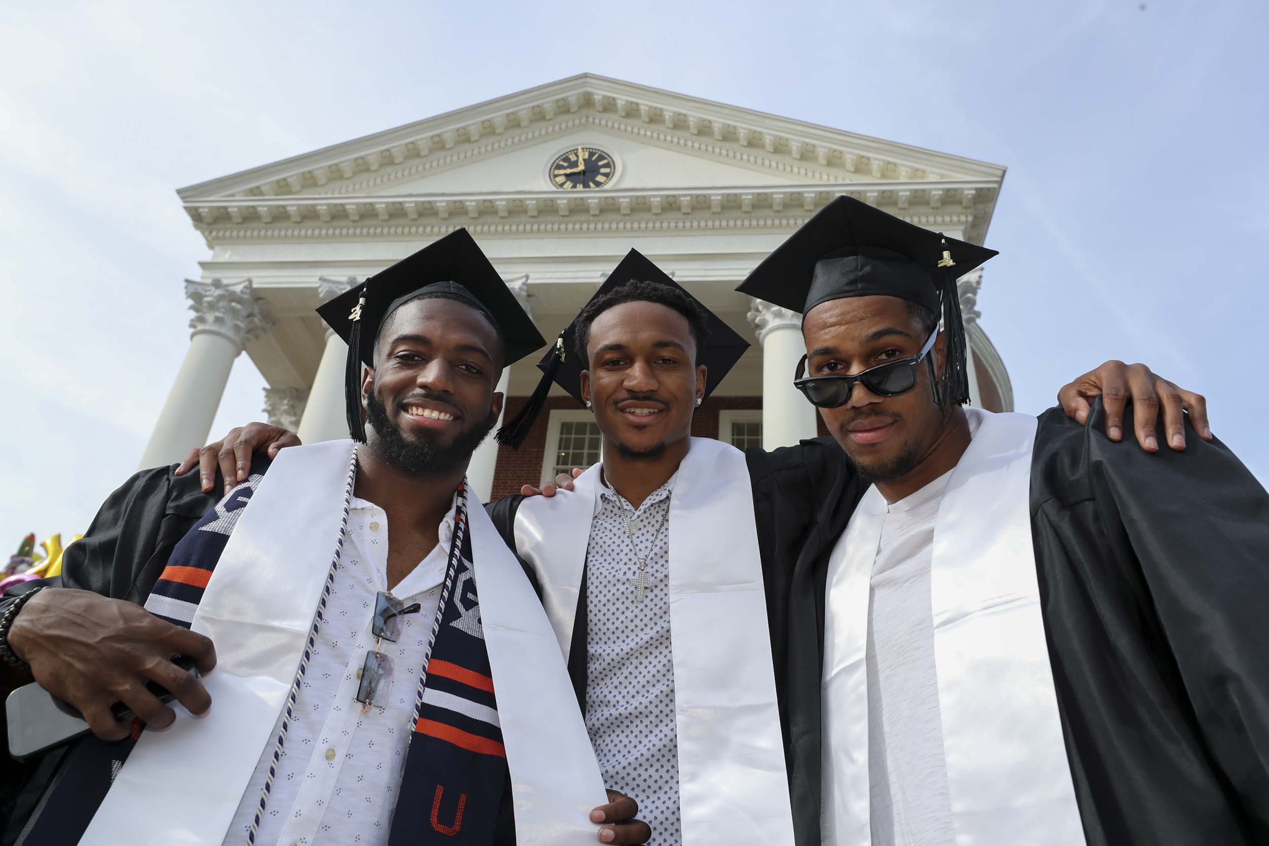 Three graduates stand in front of the Town Hall building wrapping their arms around each other shoulders for a picture.