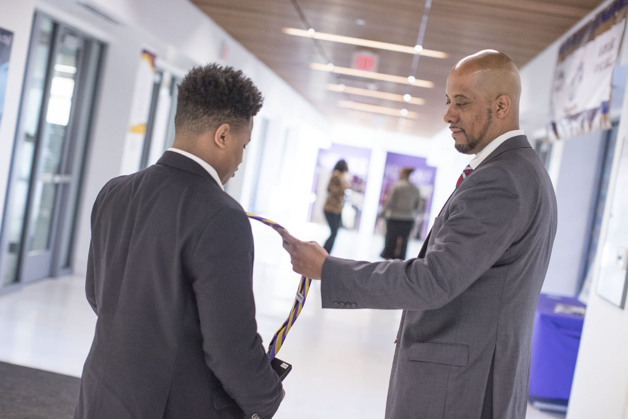 Two people dressed in suits talk in a hallway