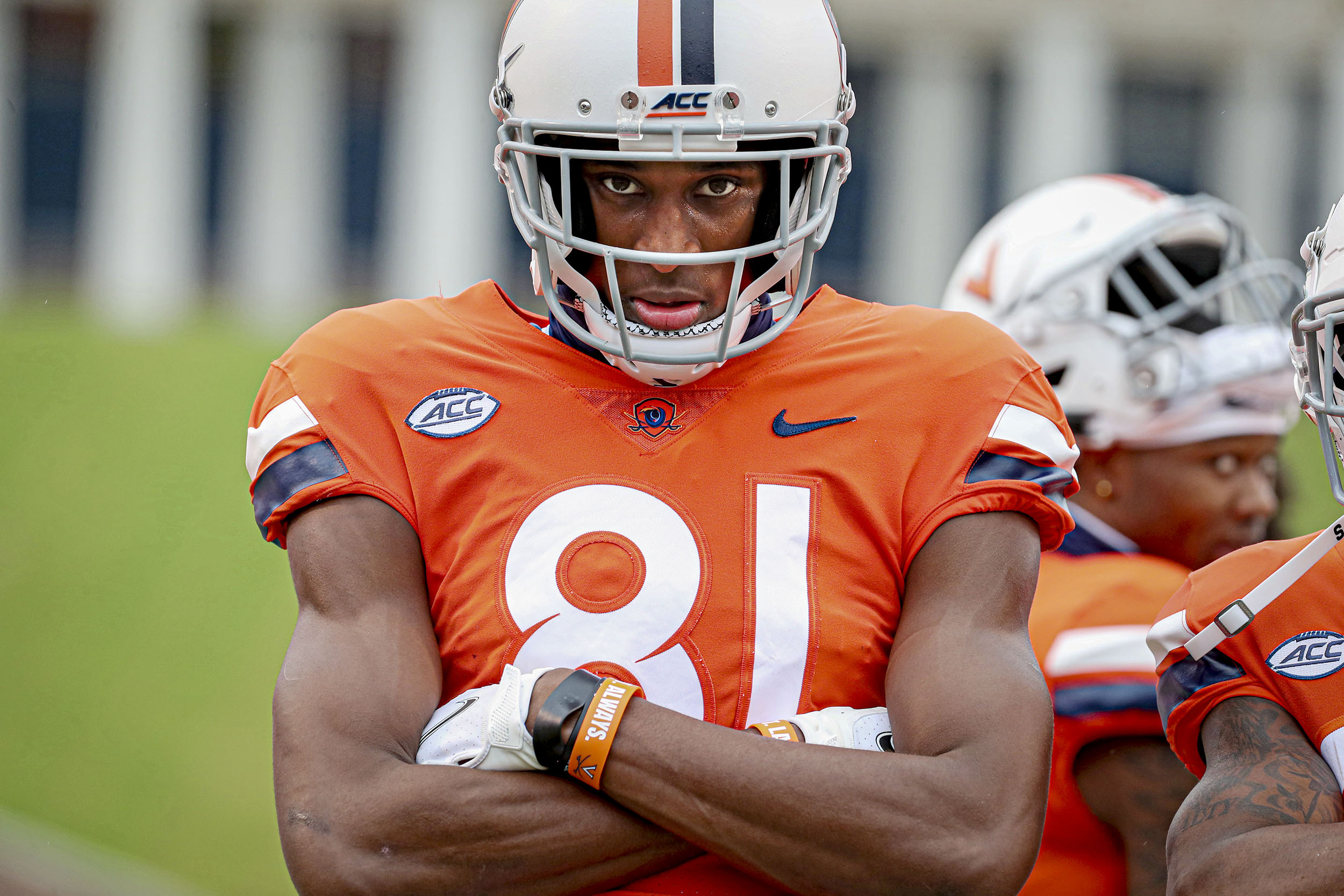 UVA mens football player dressed in orange uniform with arms crossed staring directly at the camera