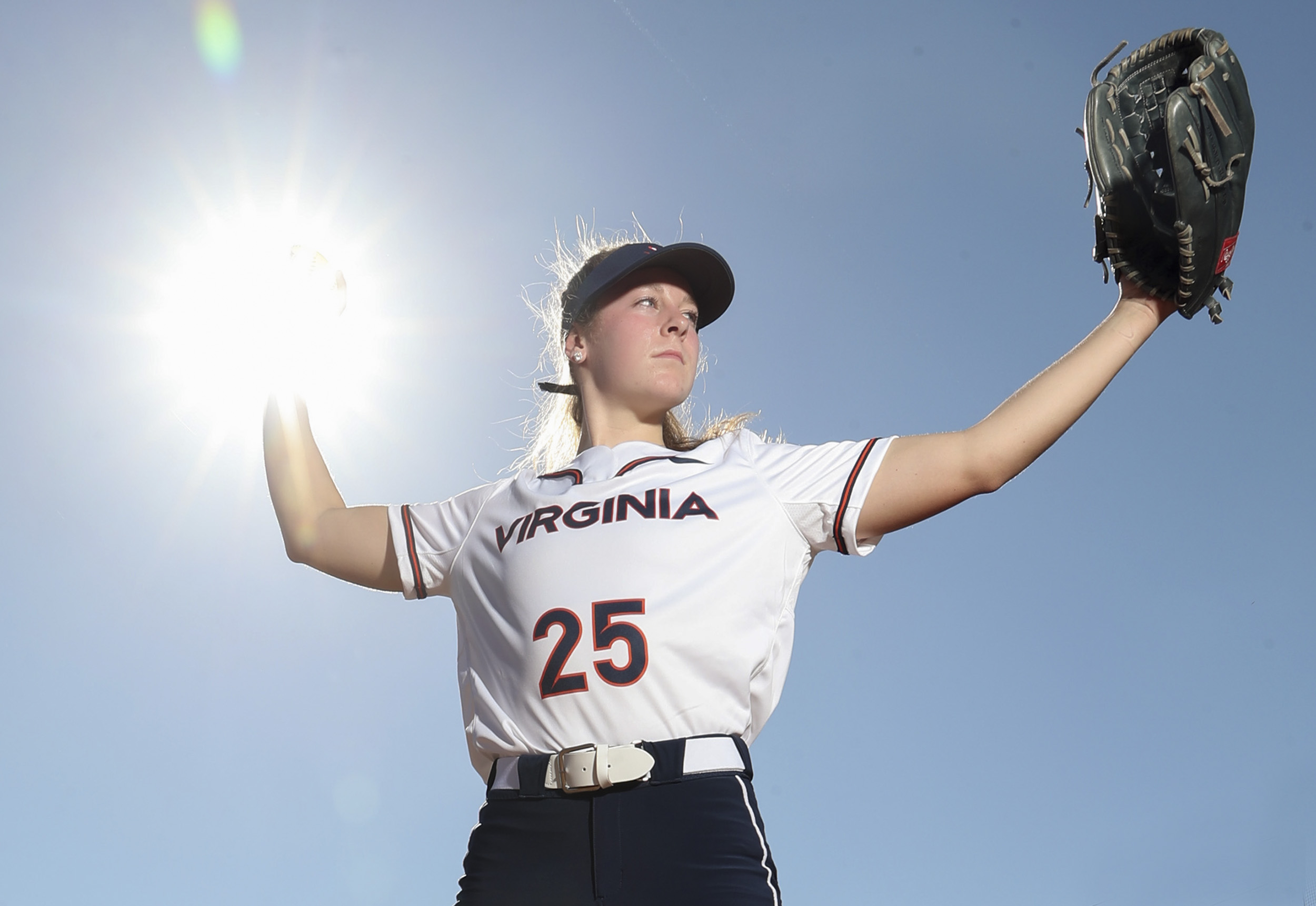 UVA Womans Softball player pitching.  the ball is directly where the sun is in the top left 