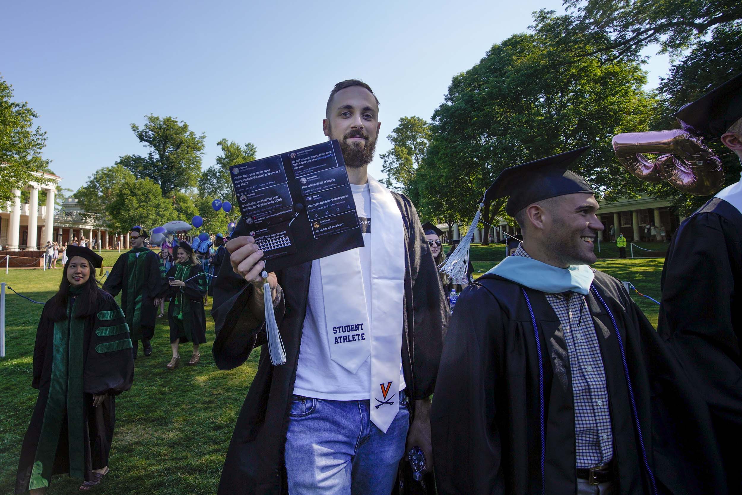 Jay Huff, UVA graduate,  holding a piece of paper with mean tweets about him as he walks across the lawn in his cap and gown
