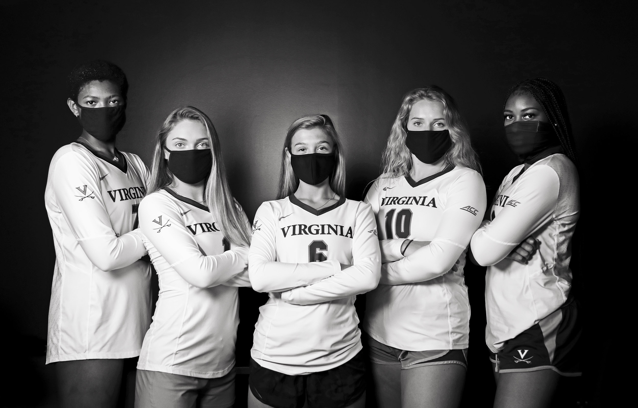 5 Women from UVA sports teams standing together with their arms crossed wearing black masks