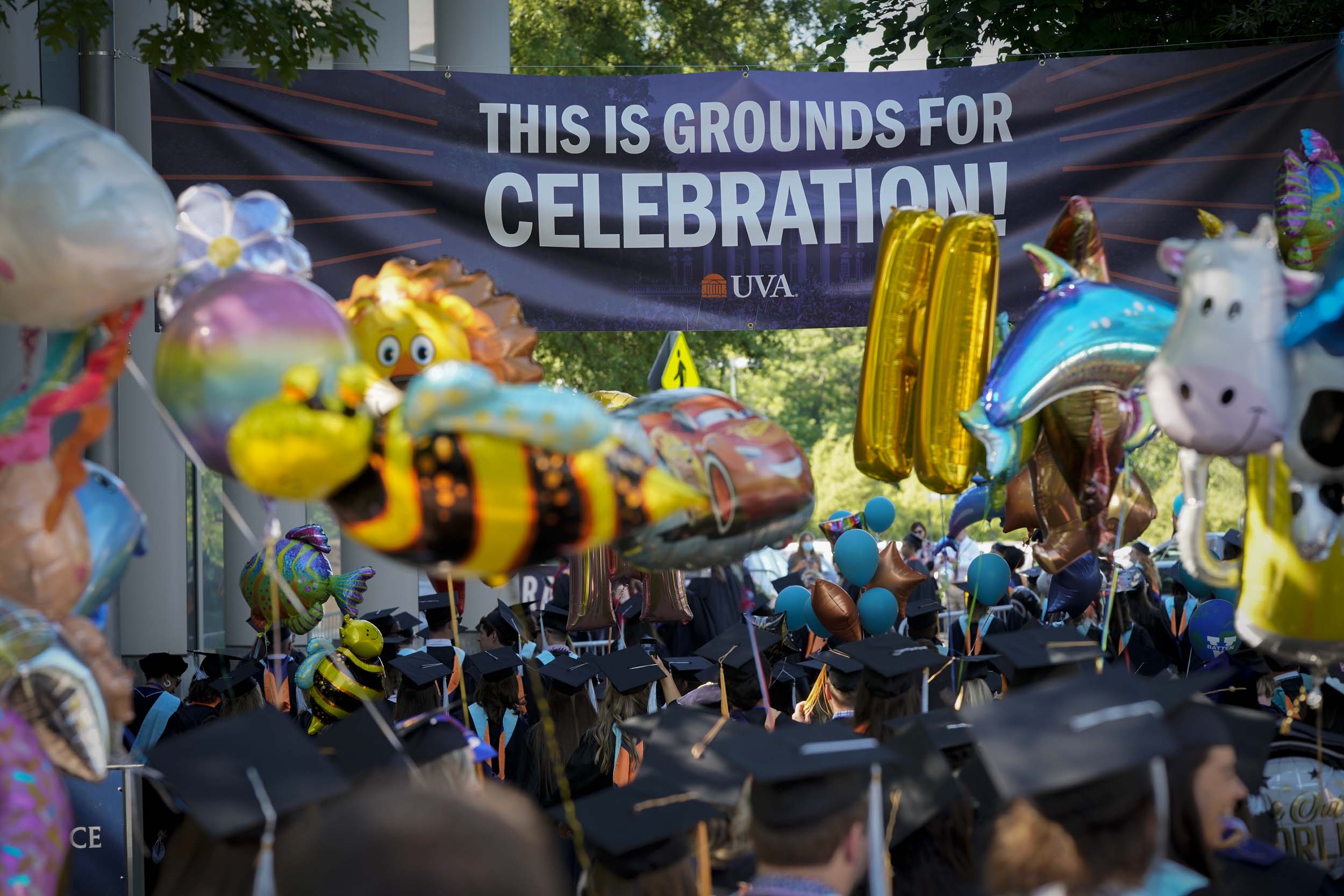 Graduates walking under a banner that reads This is the grounds for celebration