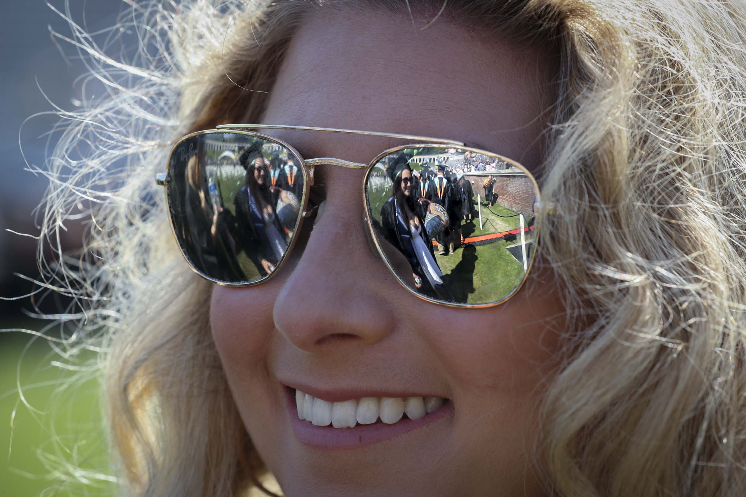 Woman smiling as you see the reflection of other graduates in their glasses