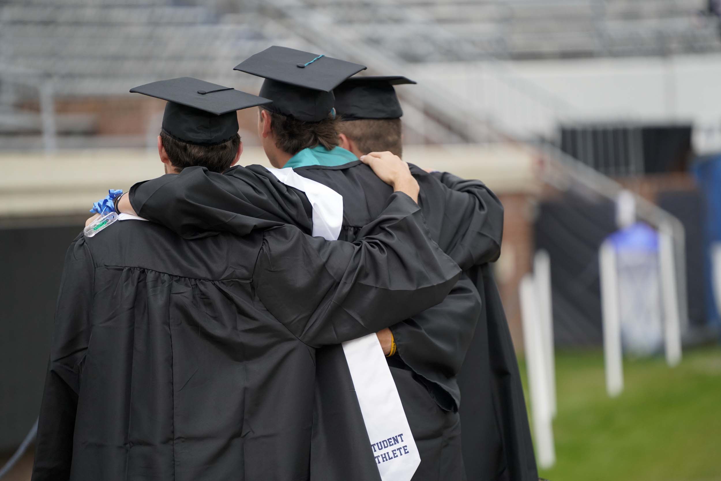 Three graduates hold each others shoulders to take a picture