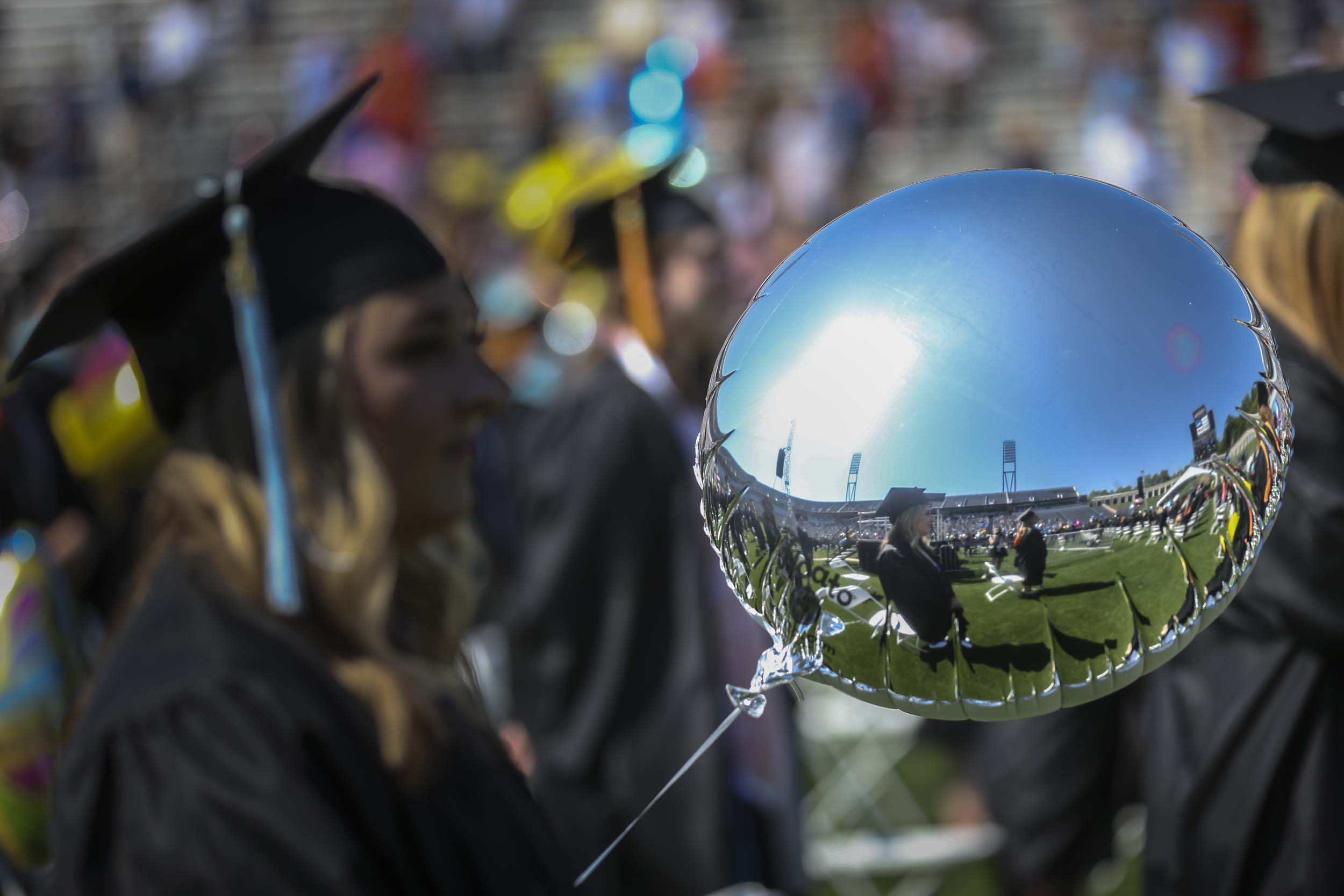 Reflection off of a shiny silver balloon of the graduates standing next to their socially distanced chairs