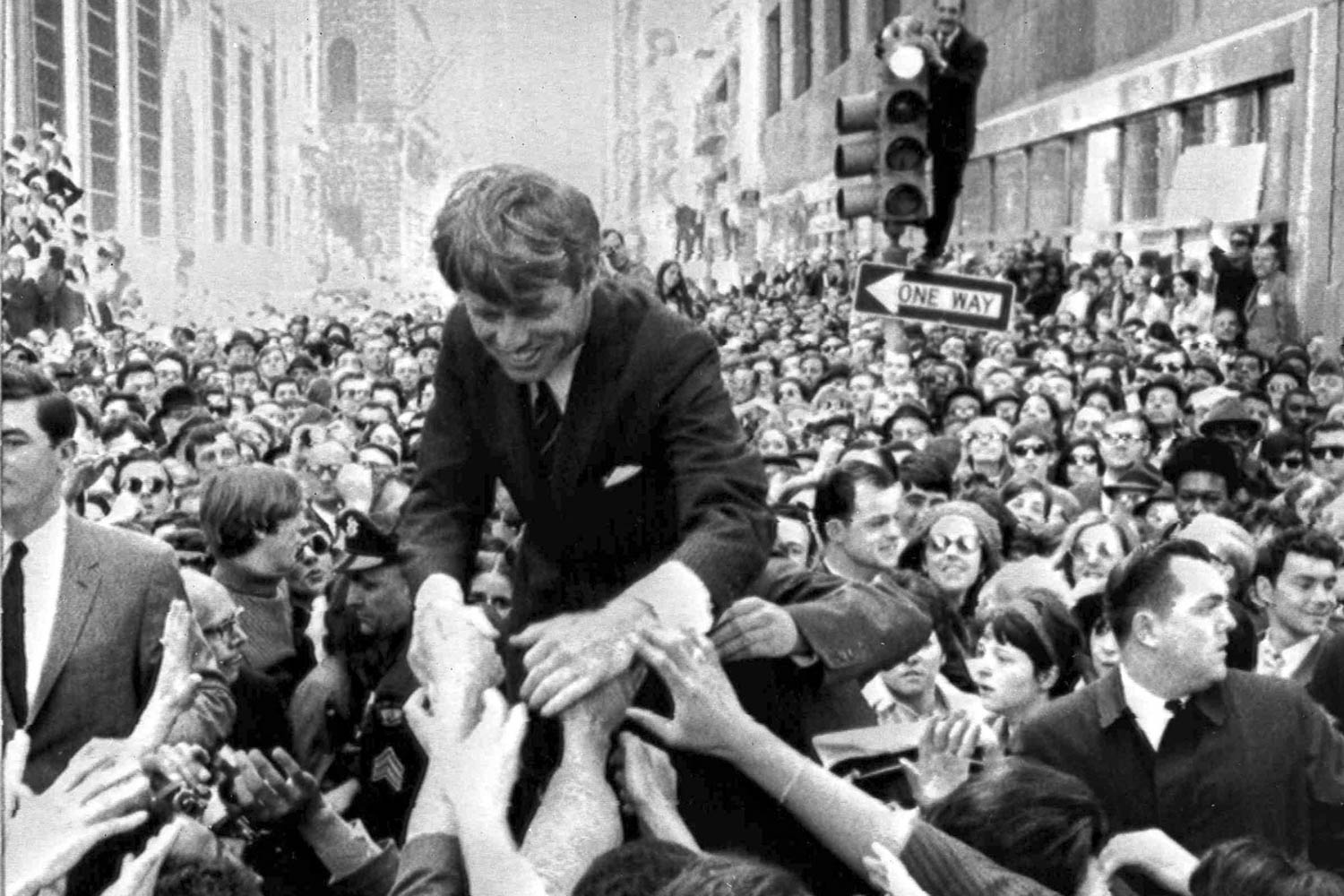 Black and white image of a JFK being lifted up above the crowd