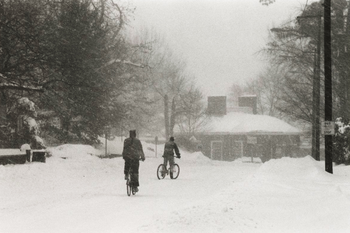 Two people riding bicycles during a snow storm