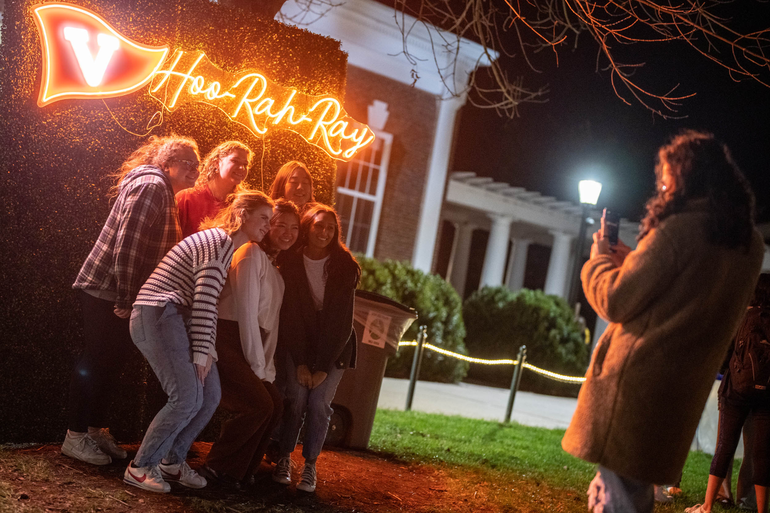 Group of students taking a group picture under the Hoo Rah ray neon sign