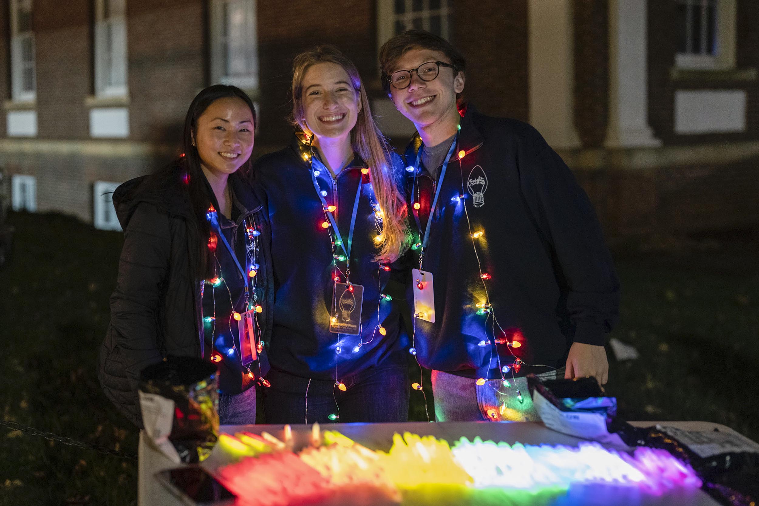 Three students wearing light up necklaces working at an event table