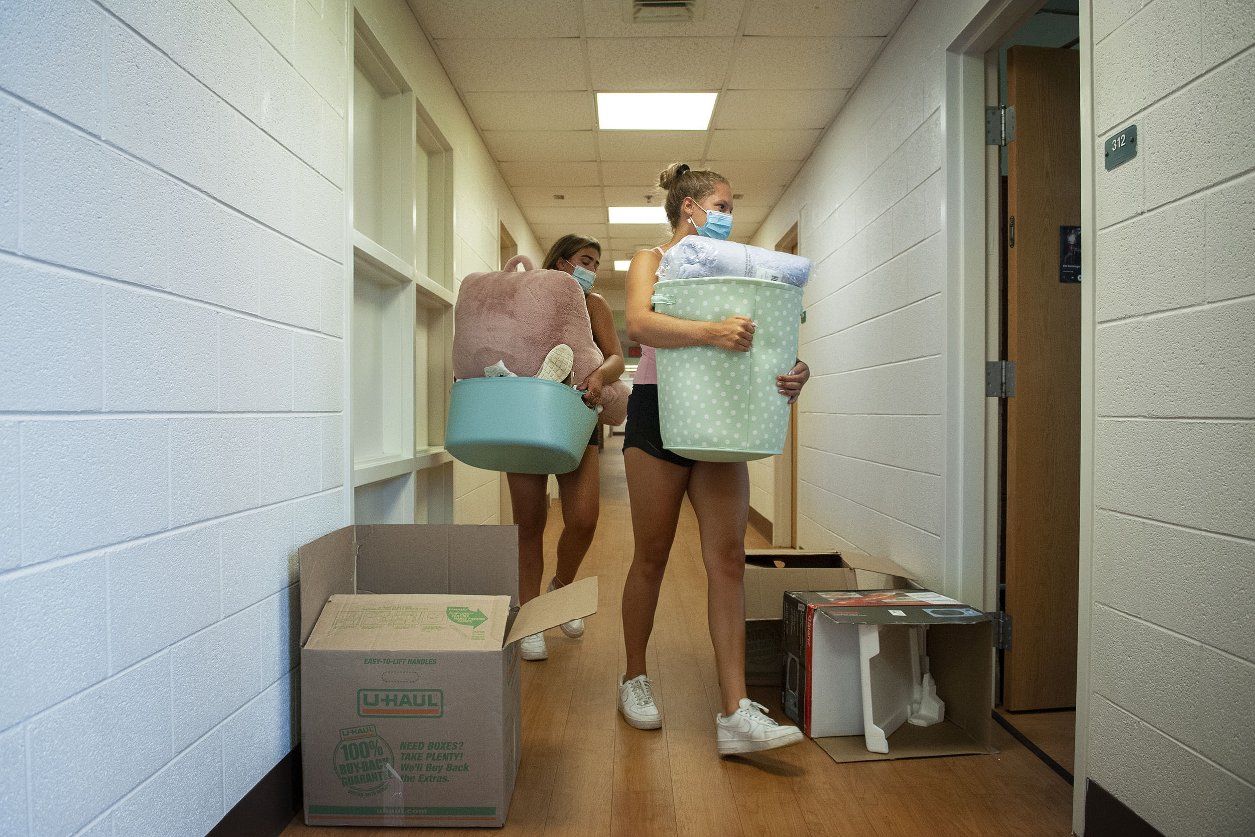 Two students walking into their dorm room with arms full of personal belongings