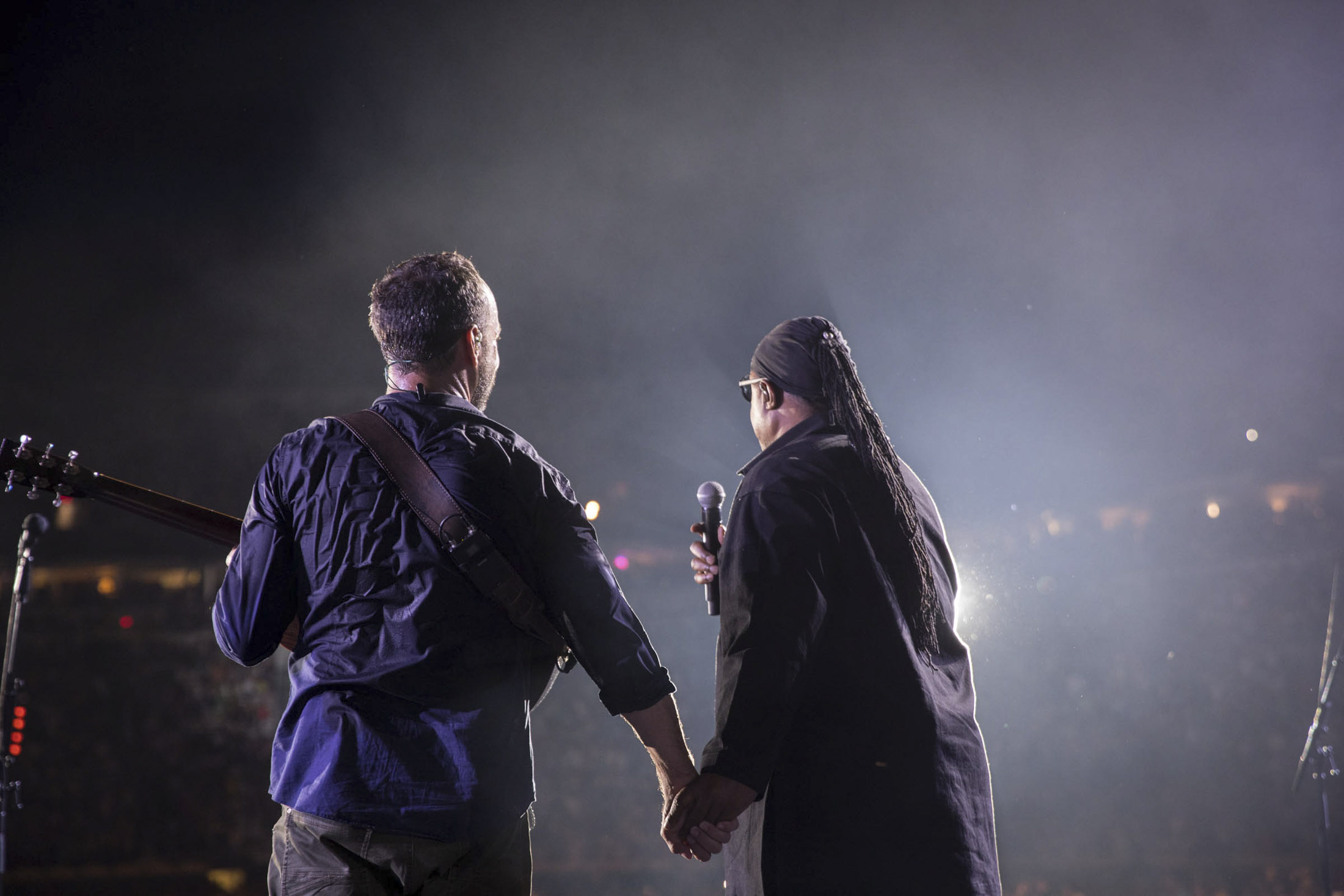 Dave Matthews holding Stevie Wonders hand on stage
