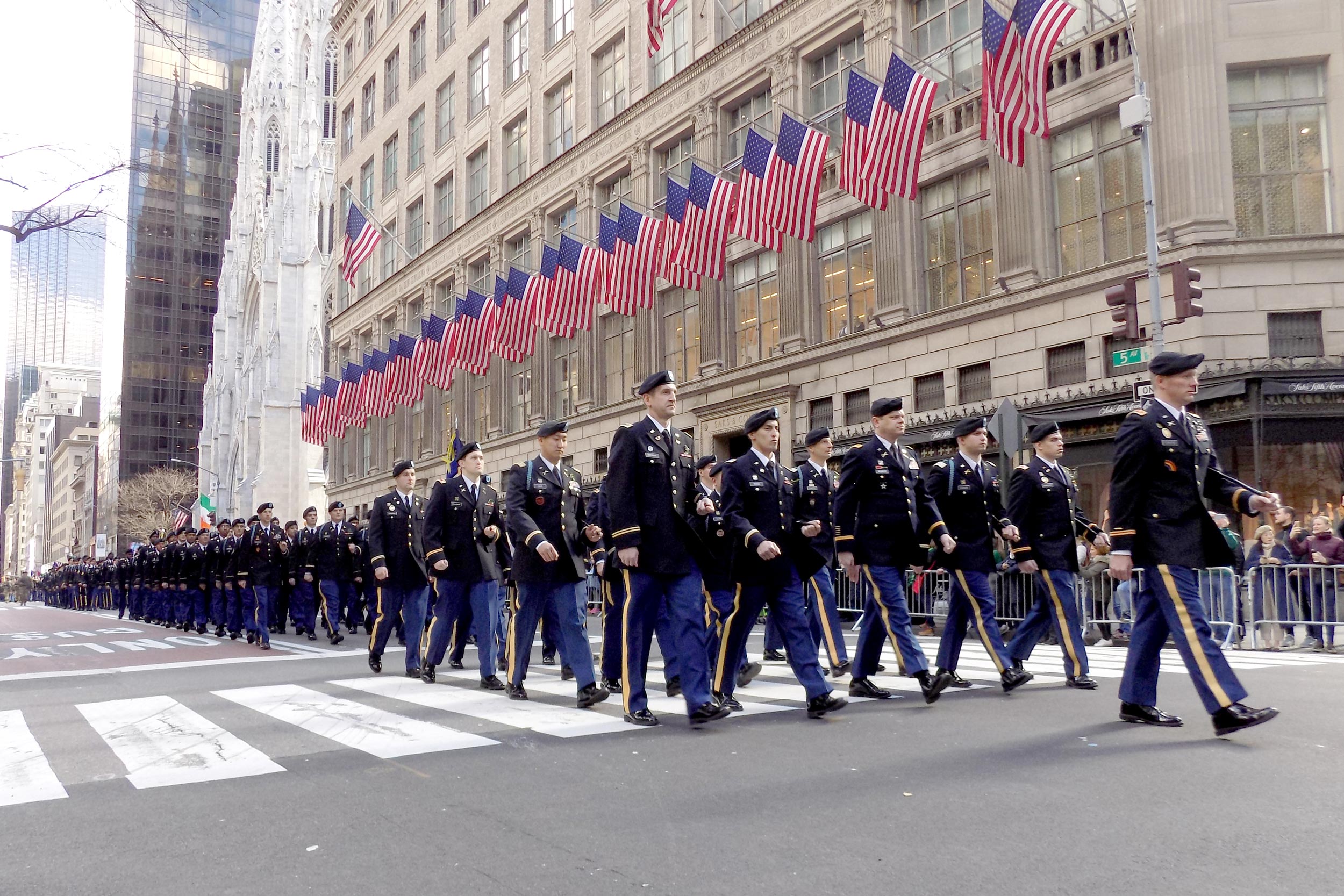 69th infantry dressed in their military uniforms marching down a New York street with USA flags above them on a building