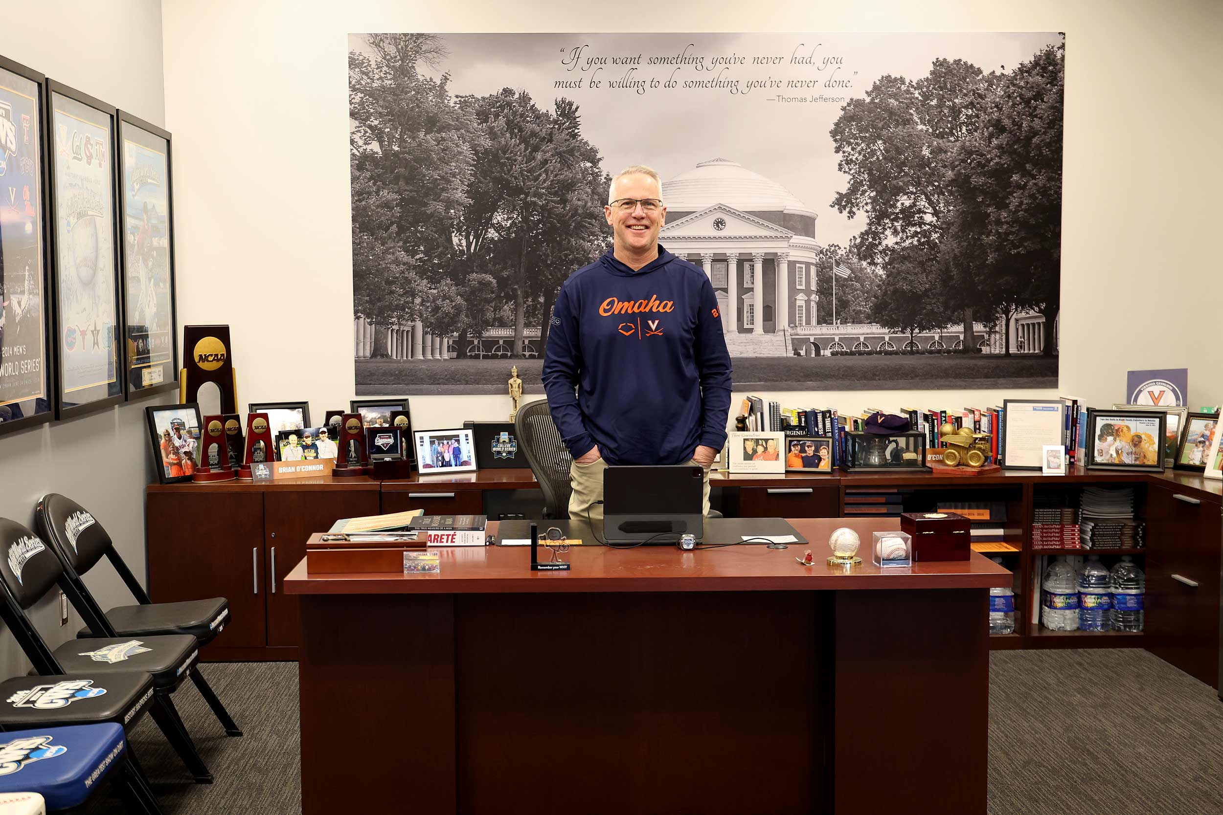 Portrait of Brian O’Connor  standing at his desk surrounded by mementos