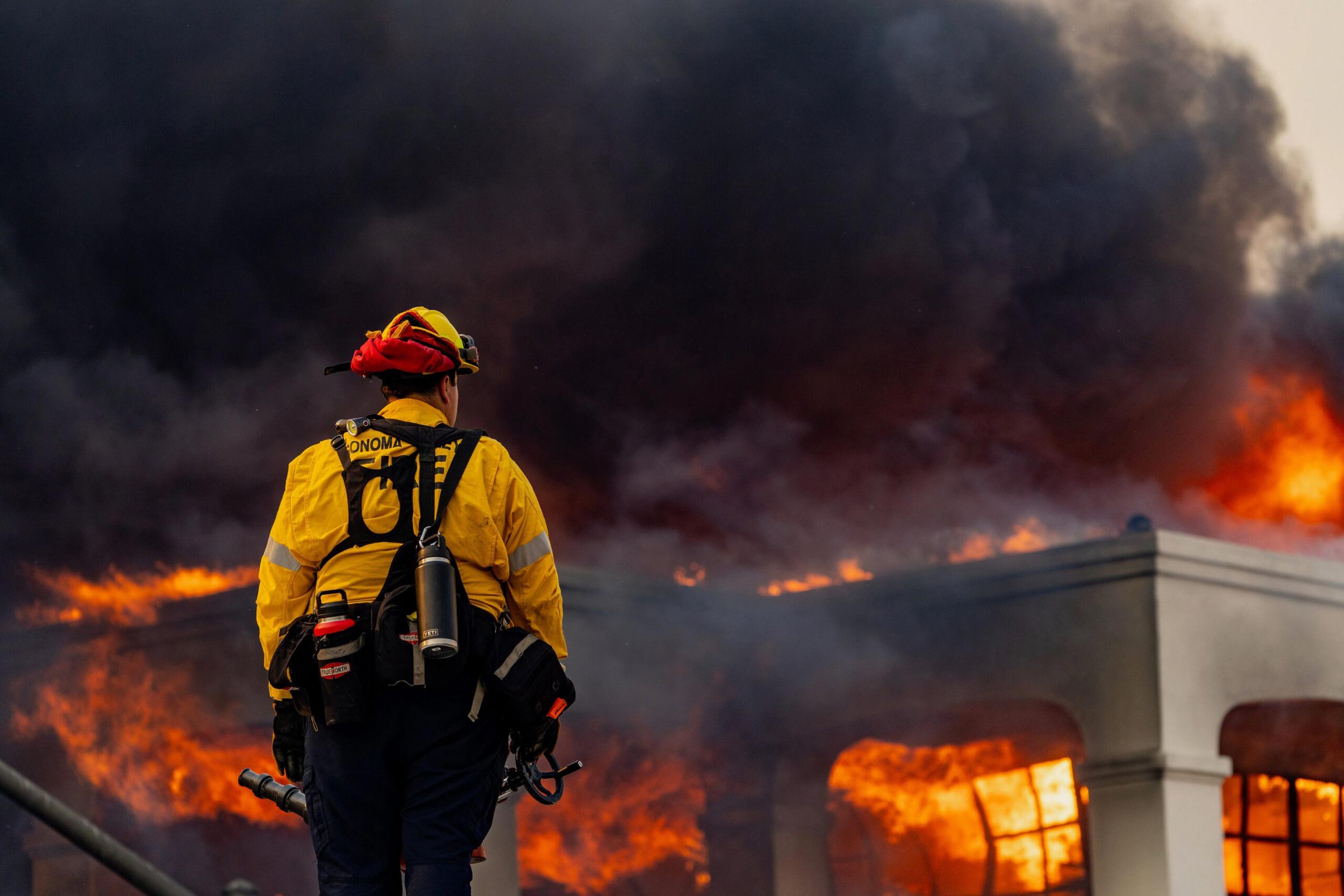 A lone firefighter stands in front of a massive fire in California