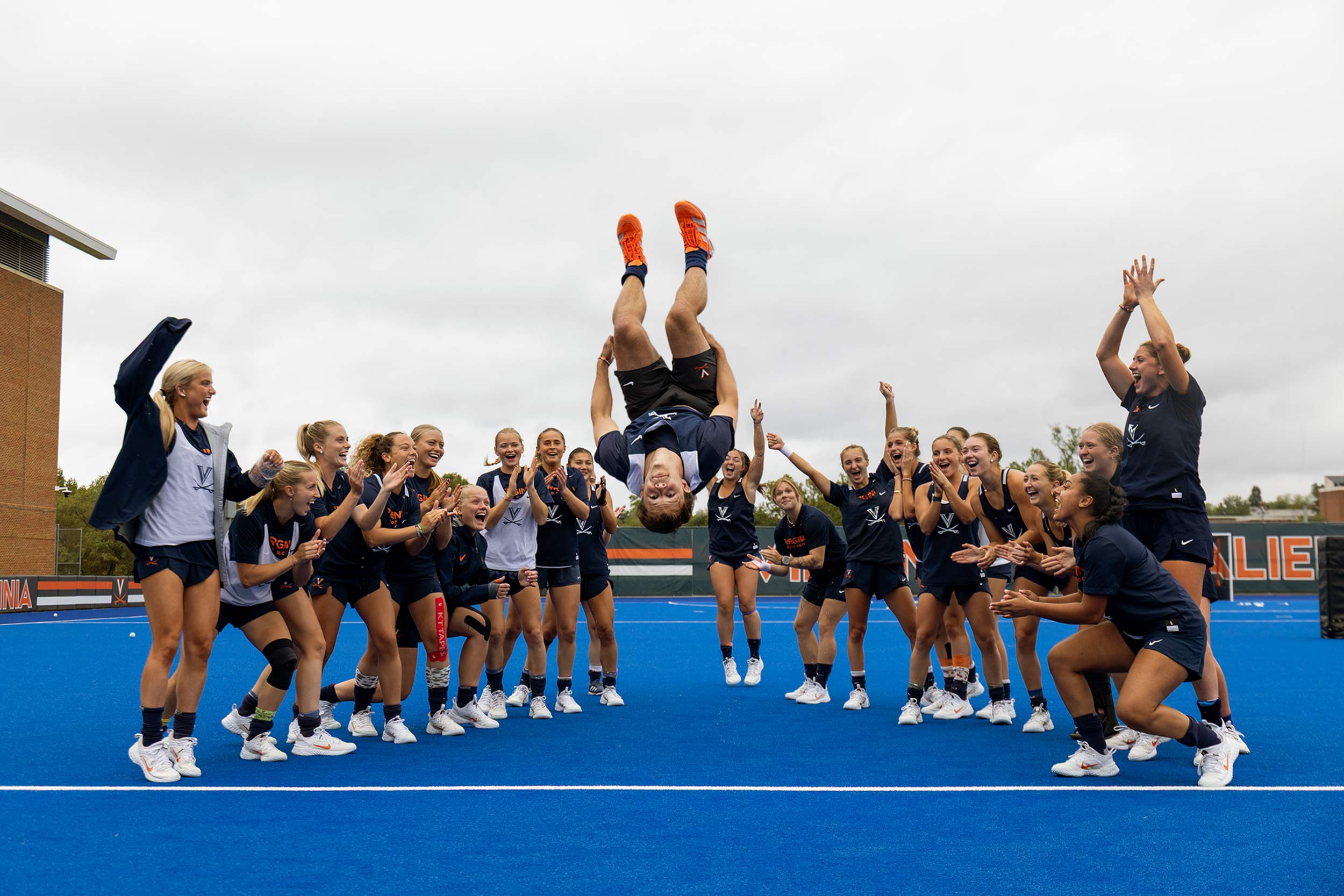 Charlie Webb mid back flip surrounded by members of the UVA field hockey team