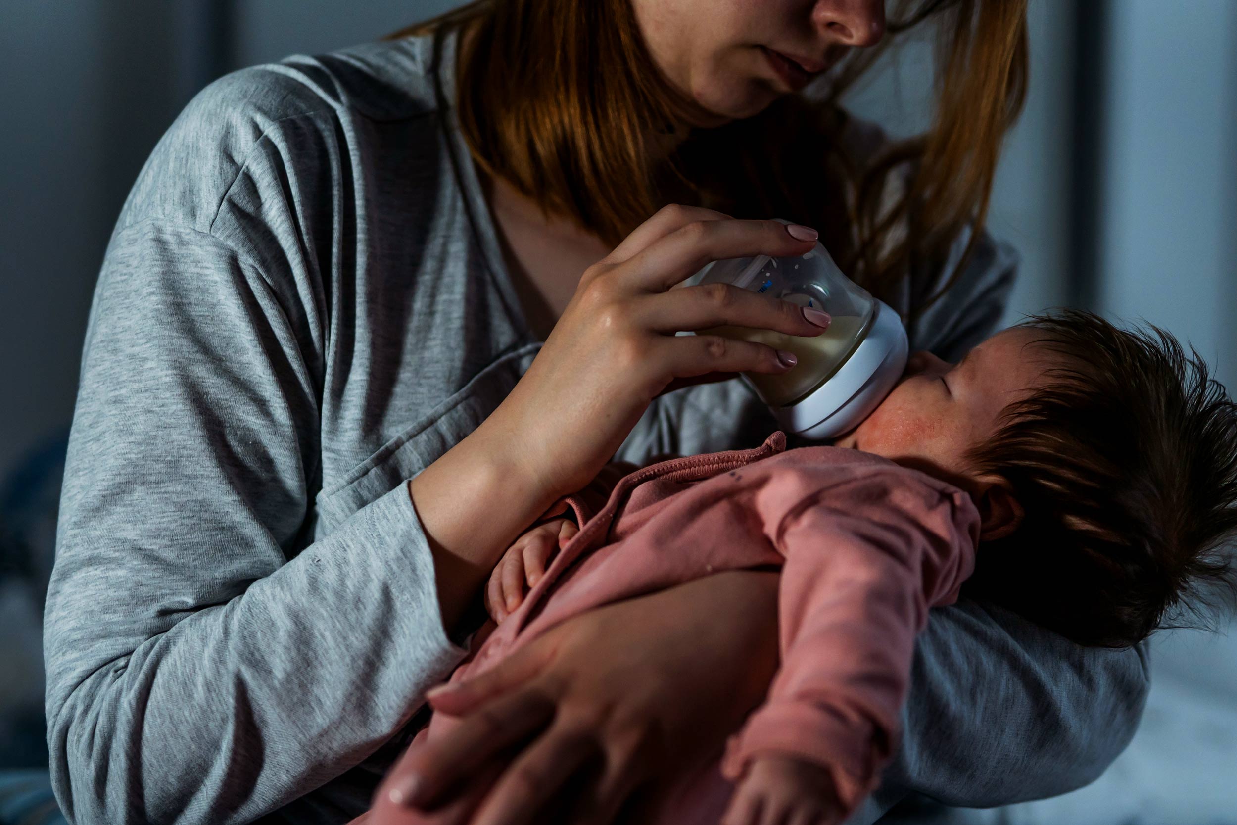 Portrait of a mother feeding her baby with a milk bottle at night.