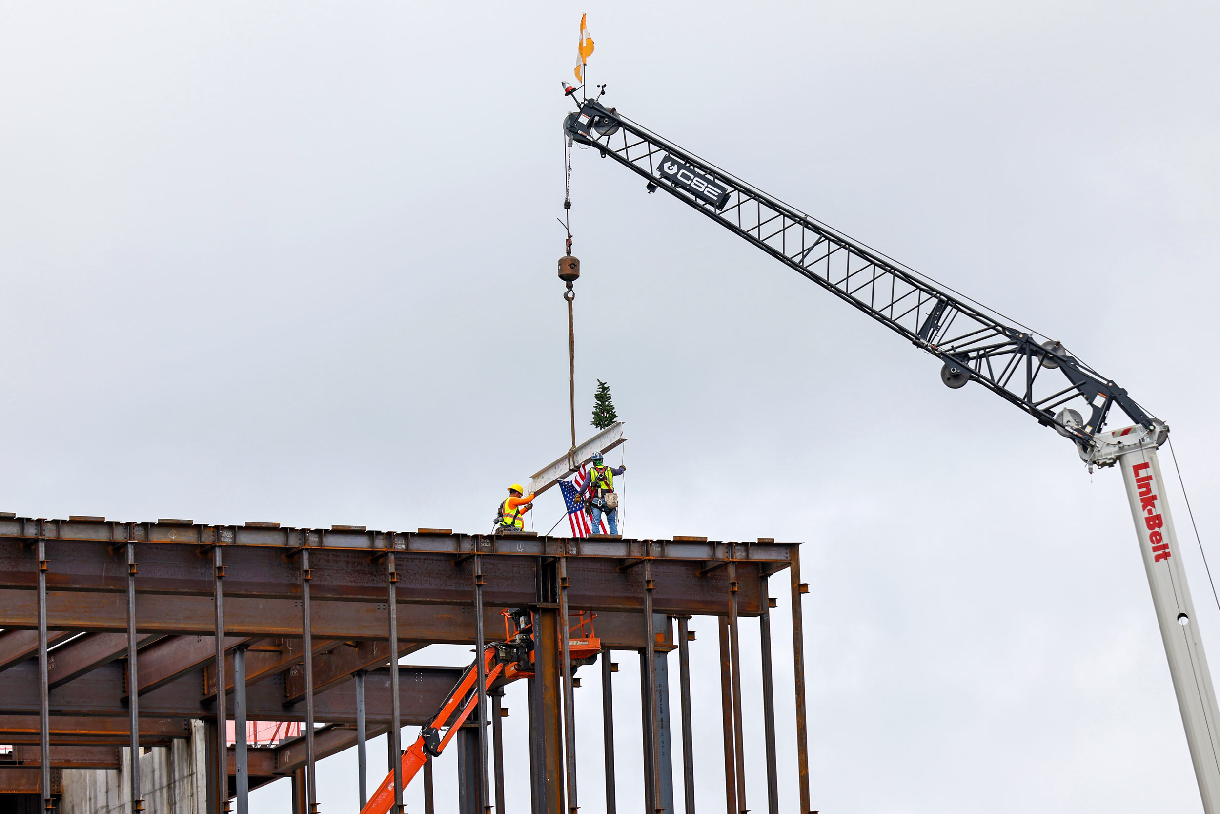 Construction workers guiding a beam being craned onto the top of a building