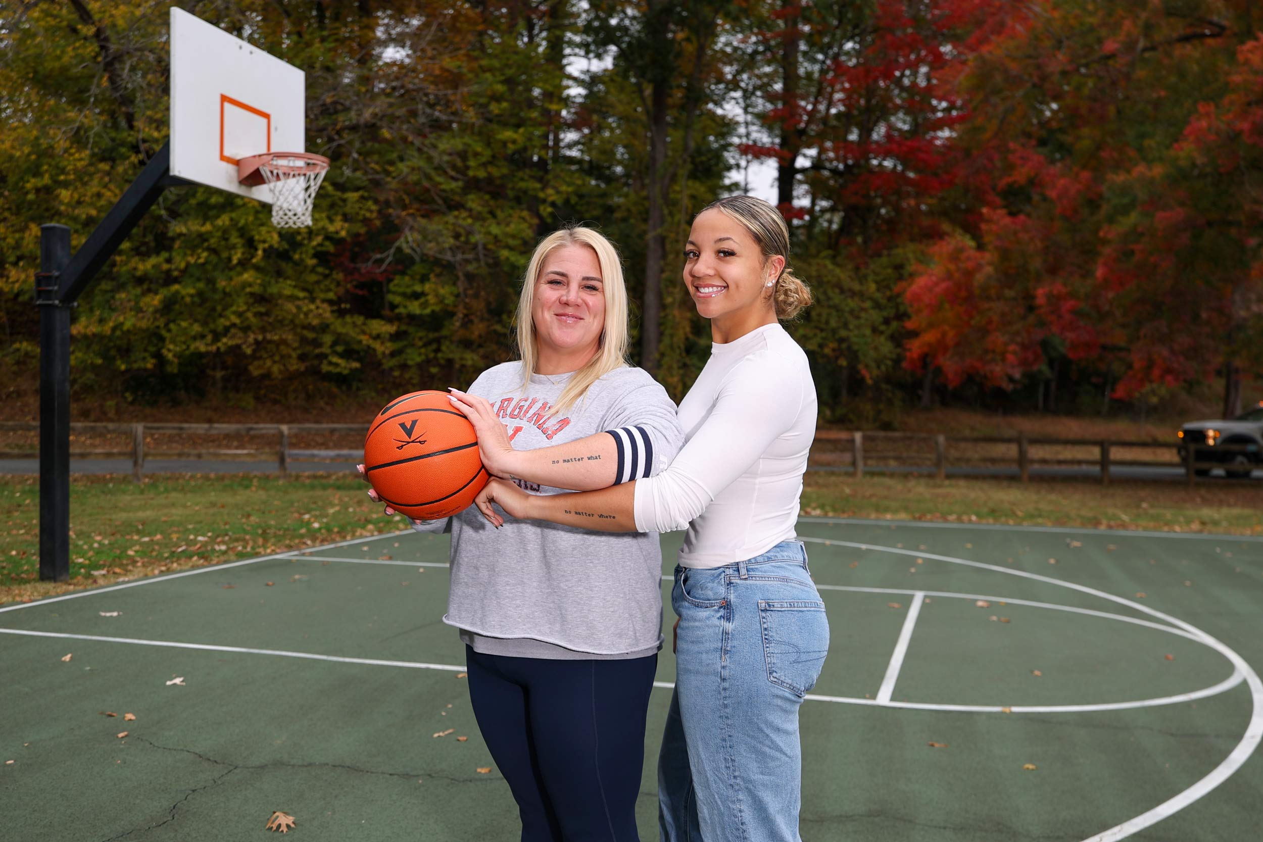 Jessica Thomas-Johnson and Kymora Johnson together on a basketball court showing their matching tattoos