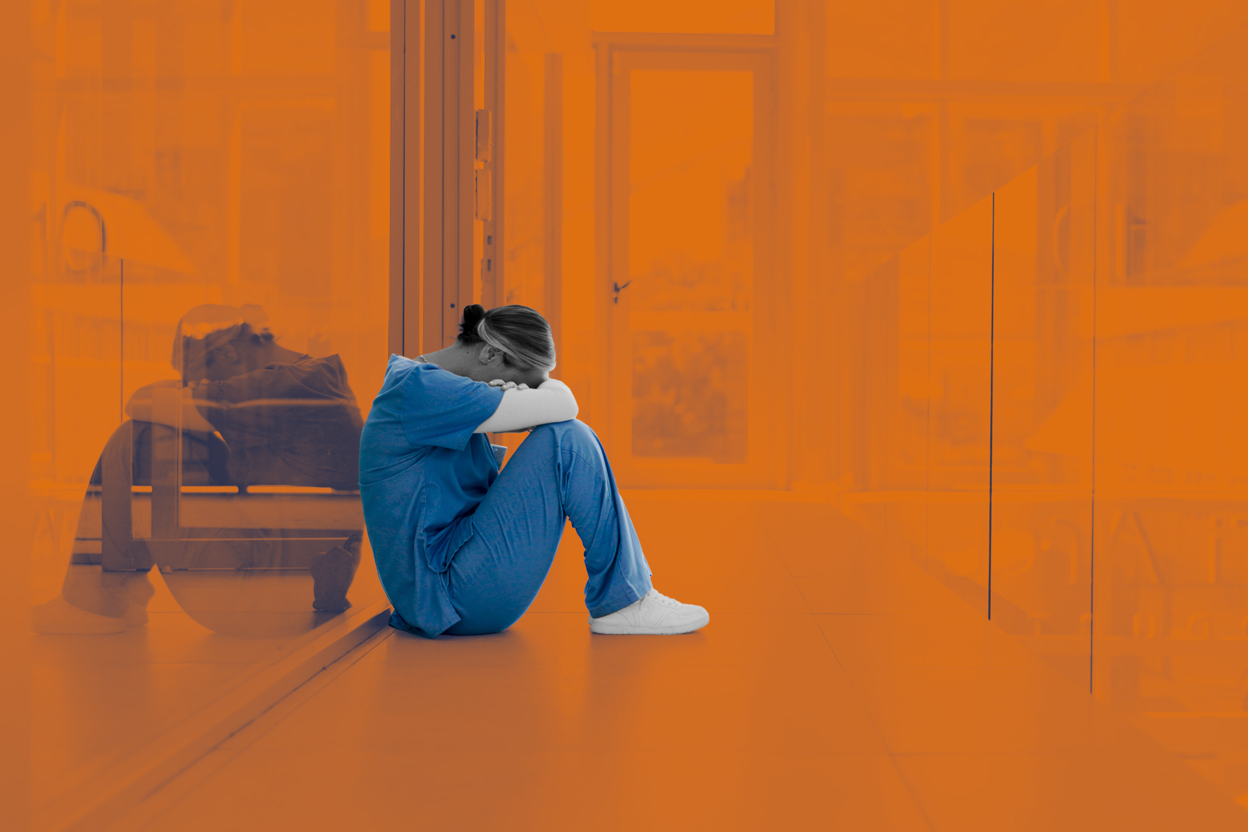 A student in scrubs sits in a hallway with their head on their knees